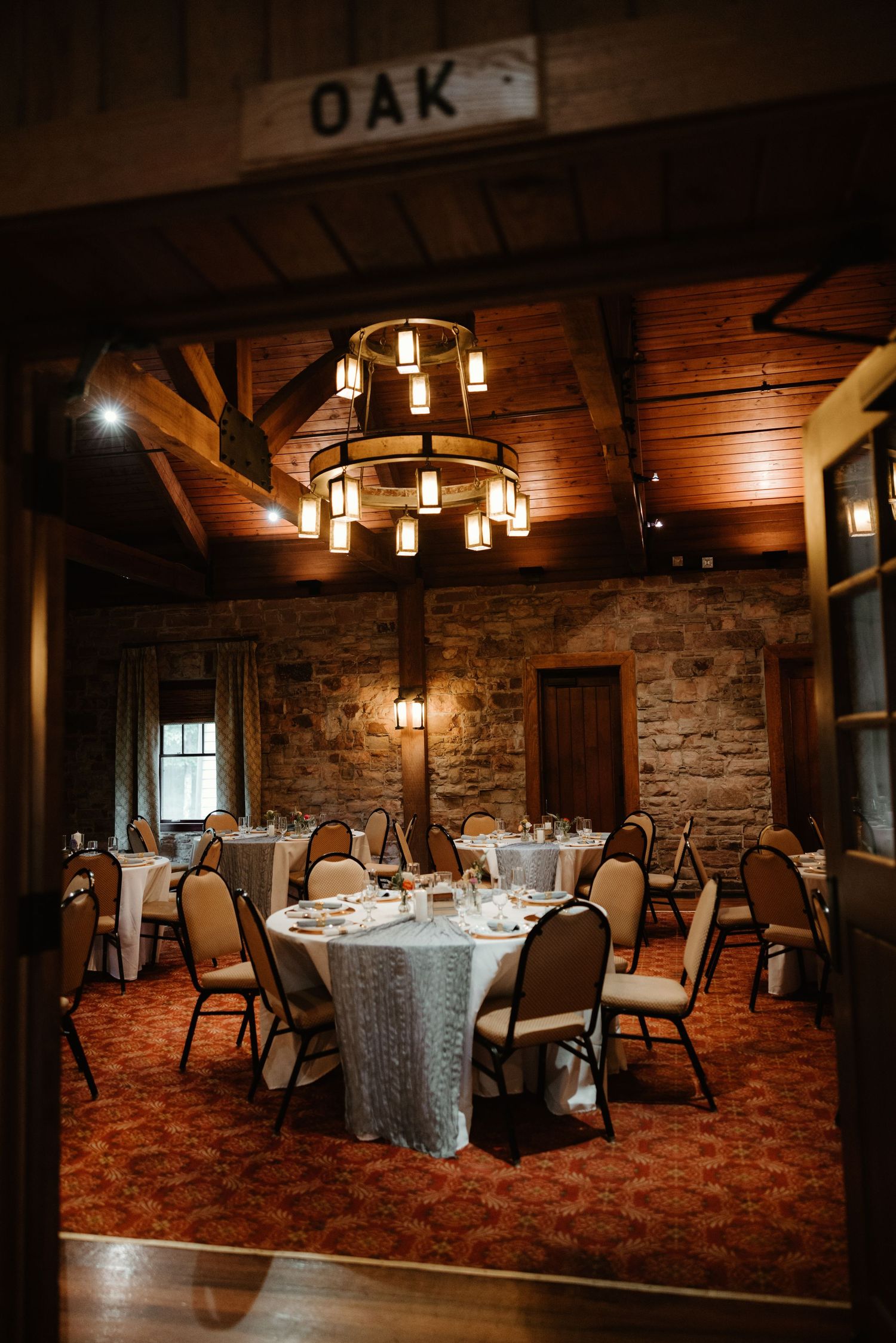 Rustic wedding reception venue with stone walls and wooden beams featuring elegant table settings and ambient lighting.