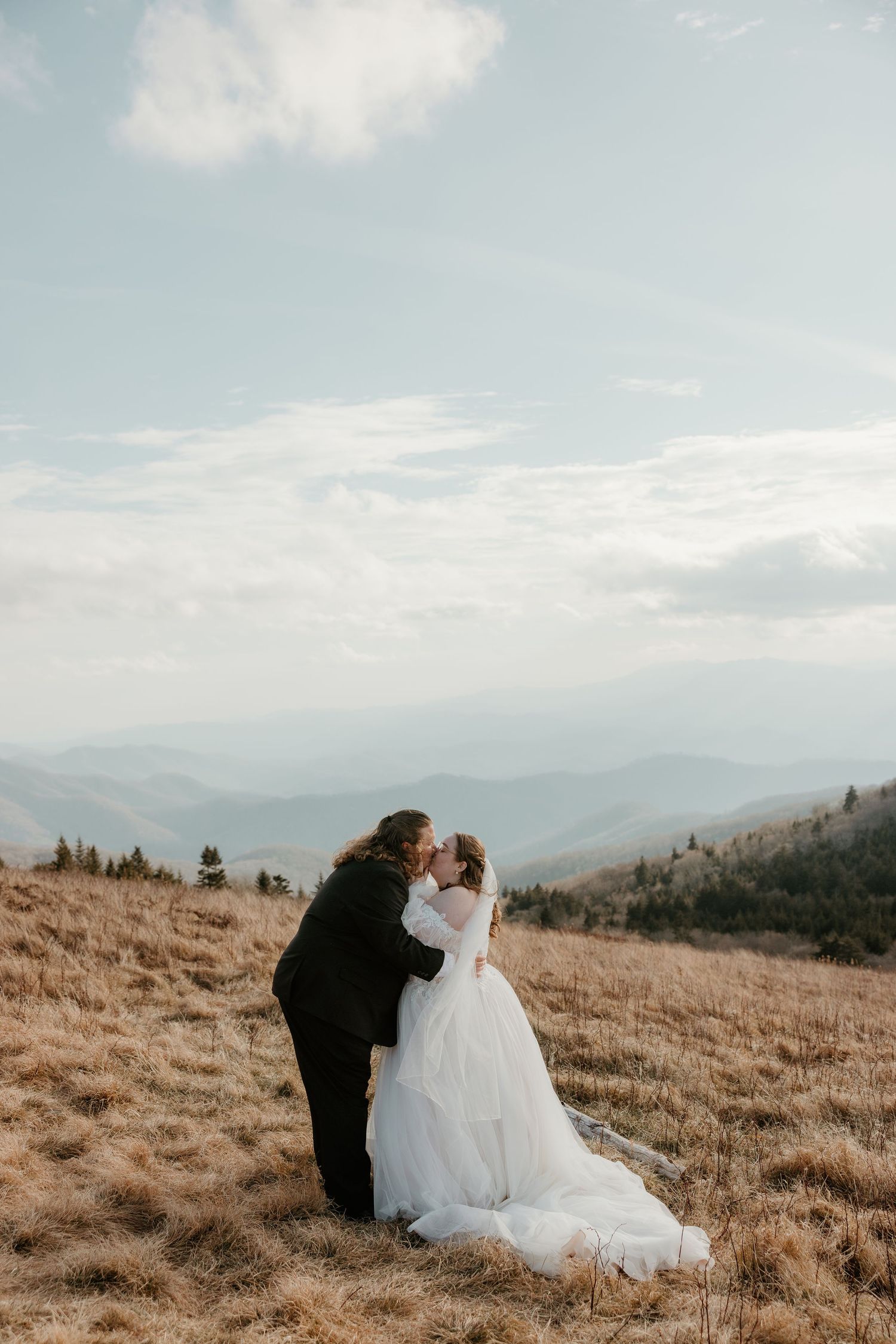 Bride and groom share a romantic kiss on a scenic mountain overlook with sweeping blue ridge mountain views.