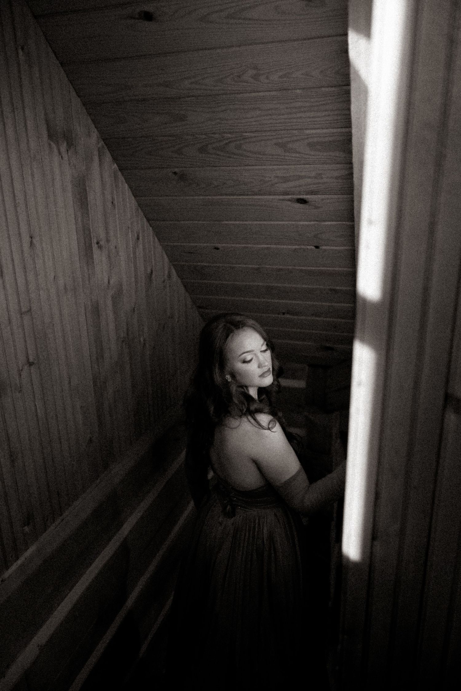 Black and white photo of a woman with closed eyes on a wooden staircase, lit by soft light from a nearby window.