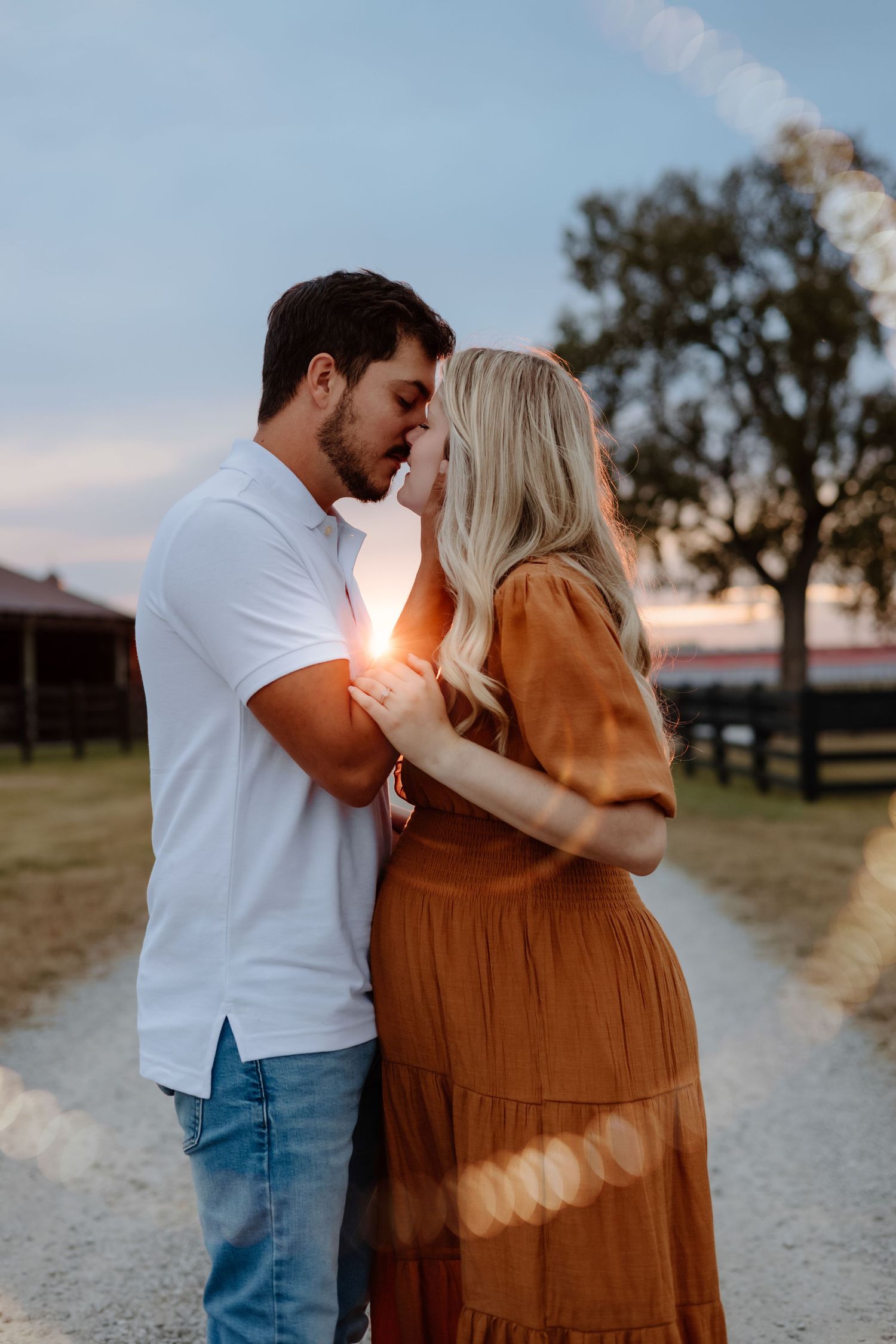 Romantic couple embracing and sharing tender moments at sunset on a rural dirt path as golden light glows around them.