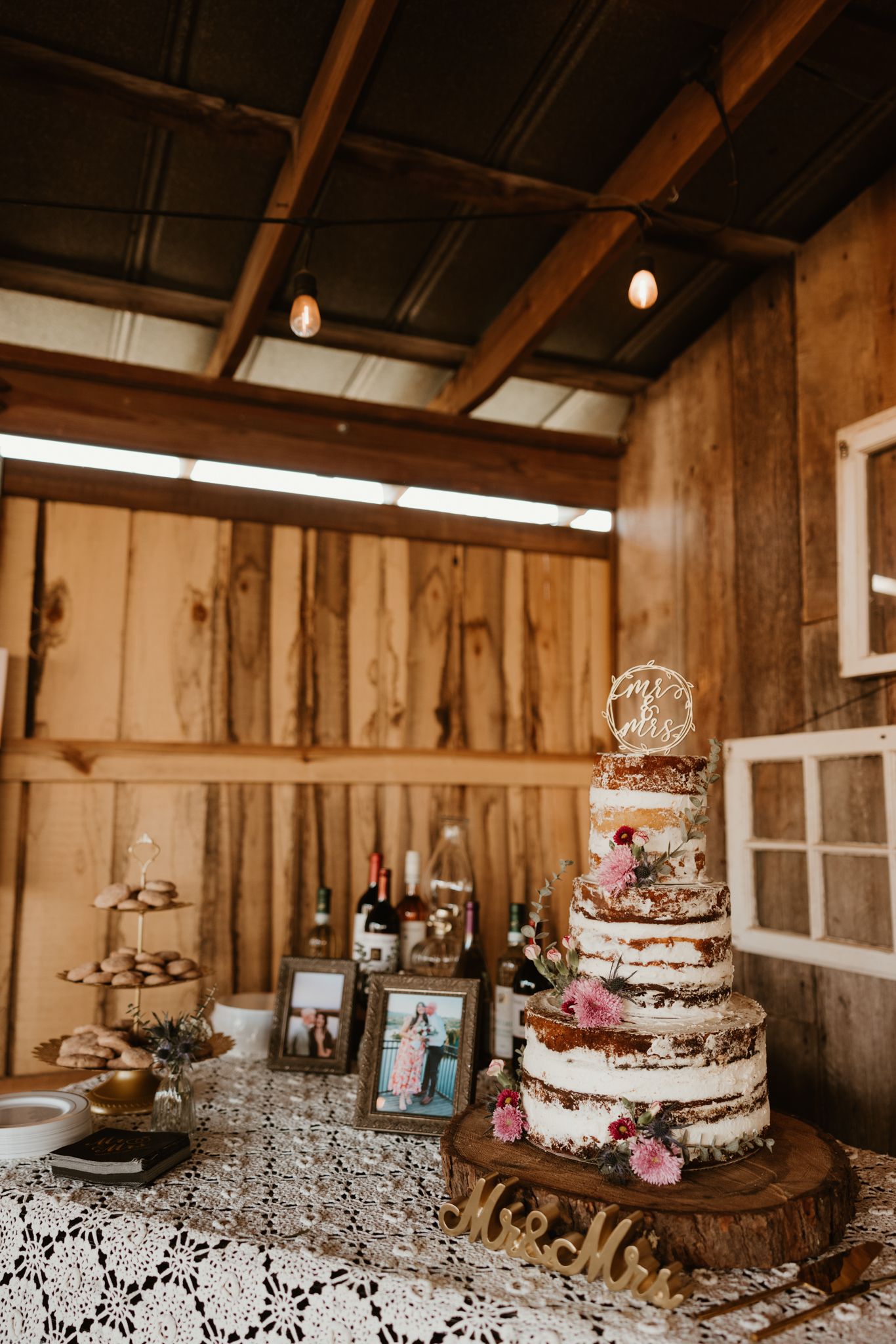 A multi-tiered naked wedding cake with floral decorations displayed on a lace-covered table.