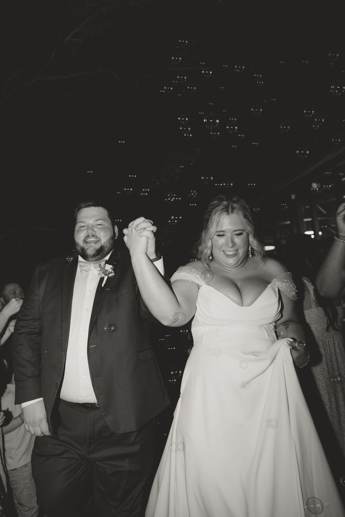 Lively nighttime wedding reception with dancing and floating bubbles in the background.