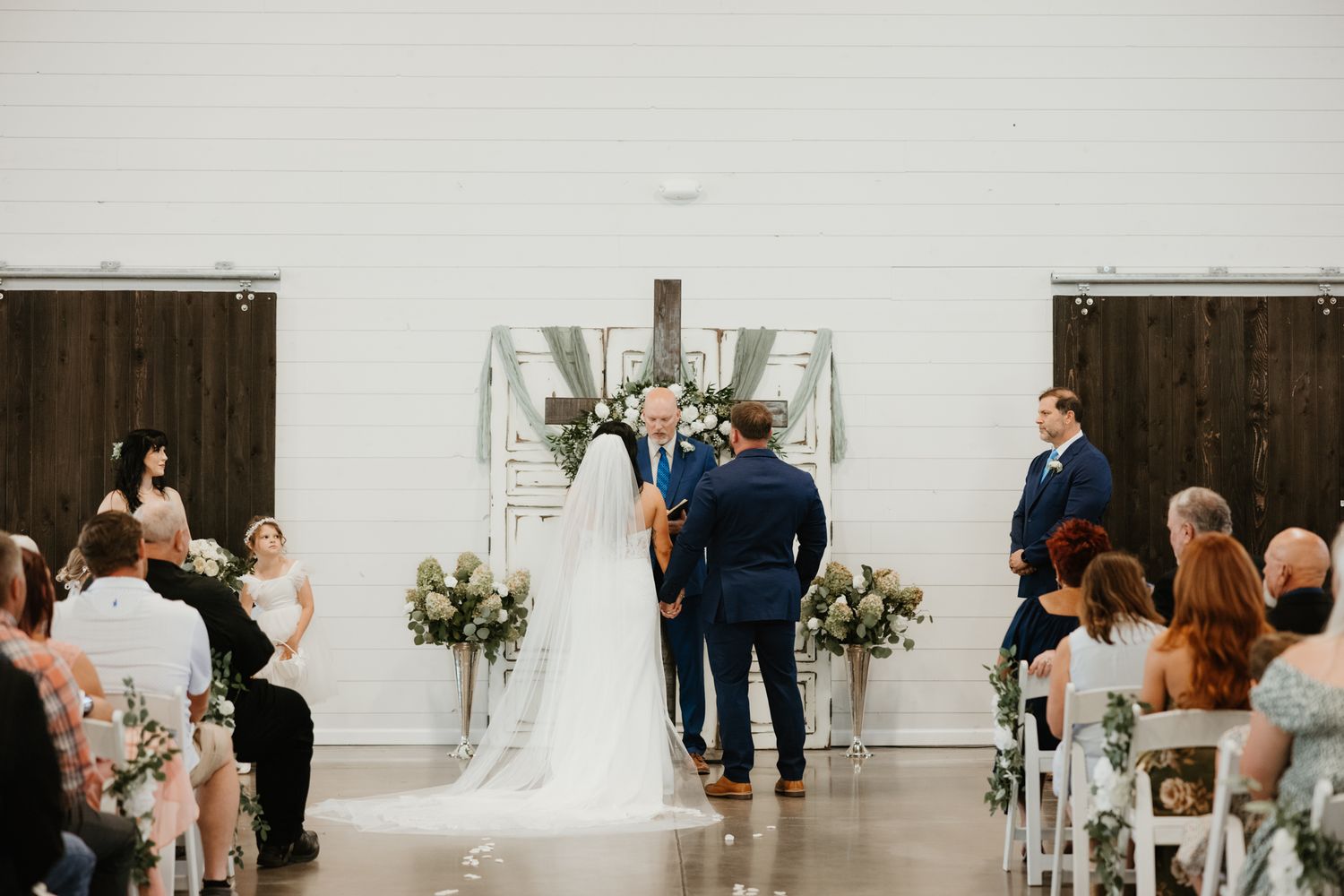 Wedding ceremony setting in white venue with guests seated in rows watching proceedings.