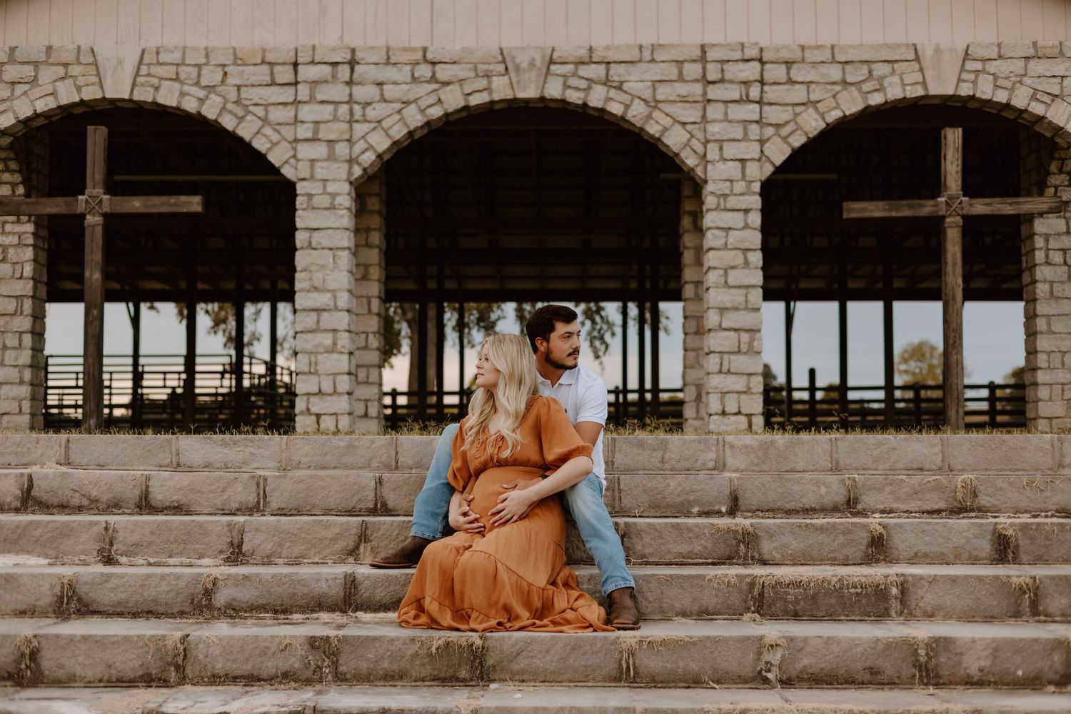 A couple sitting on stone steps with arched architecture in the background.