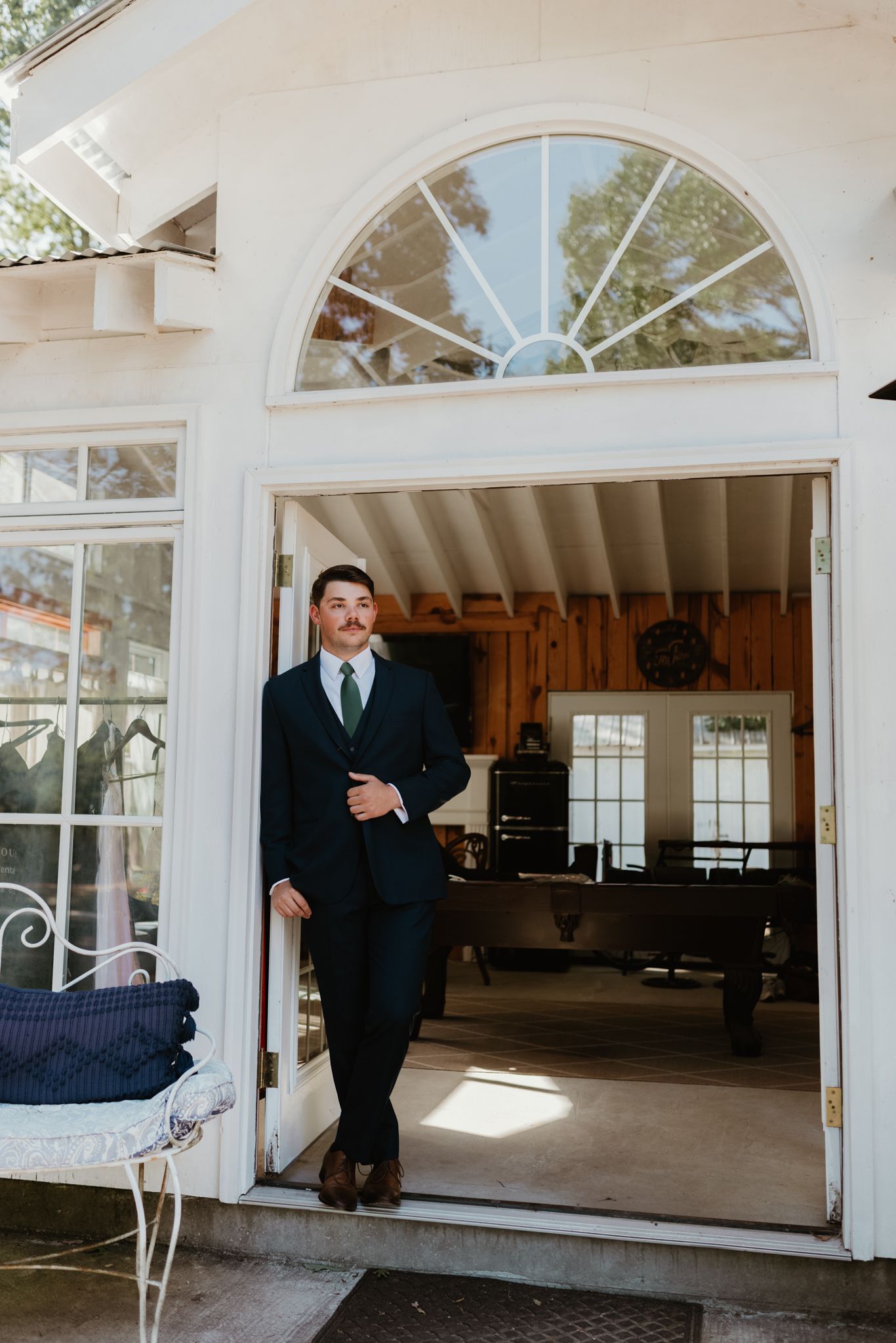 Person in navy suit standing in elegant doorway with arched window and white trim detailing.