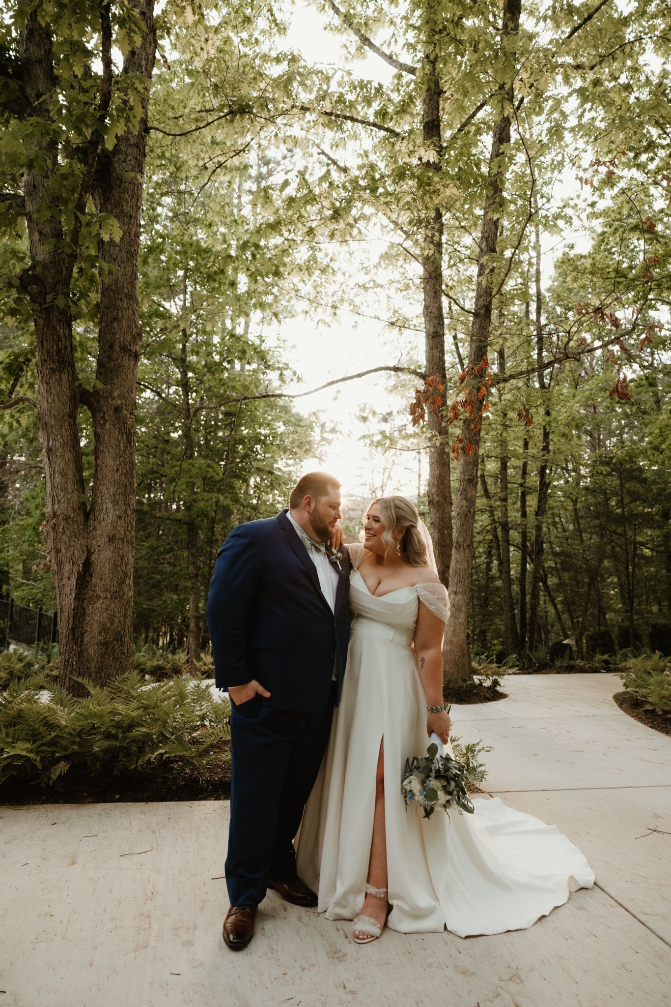 Romantic wedding couple portrait in a sunlit wooded pathway.