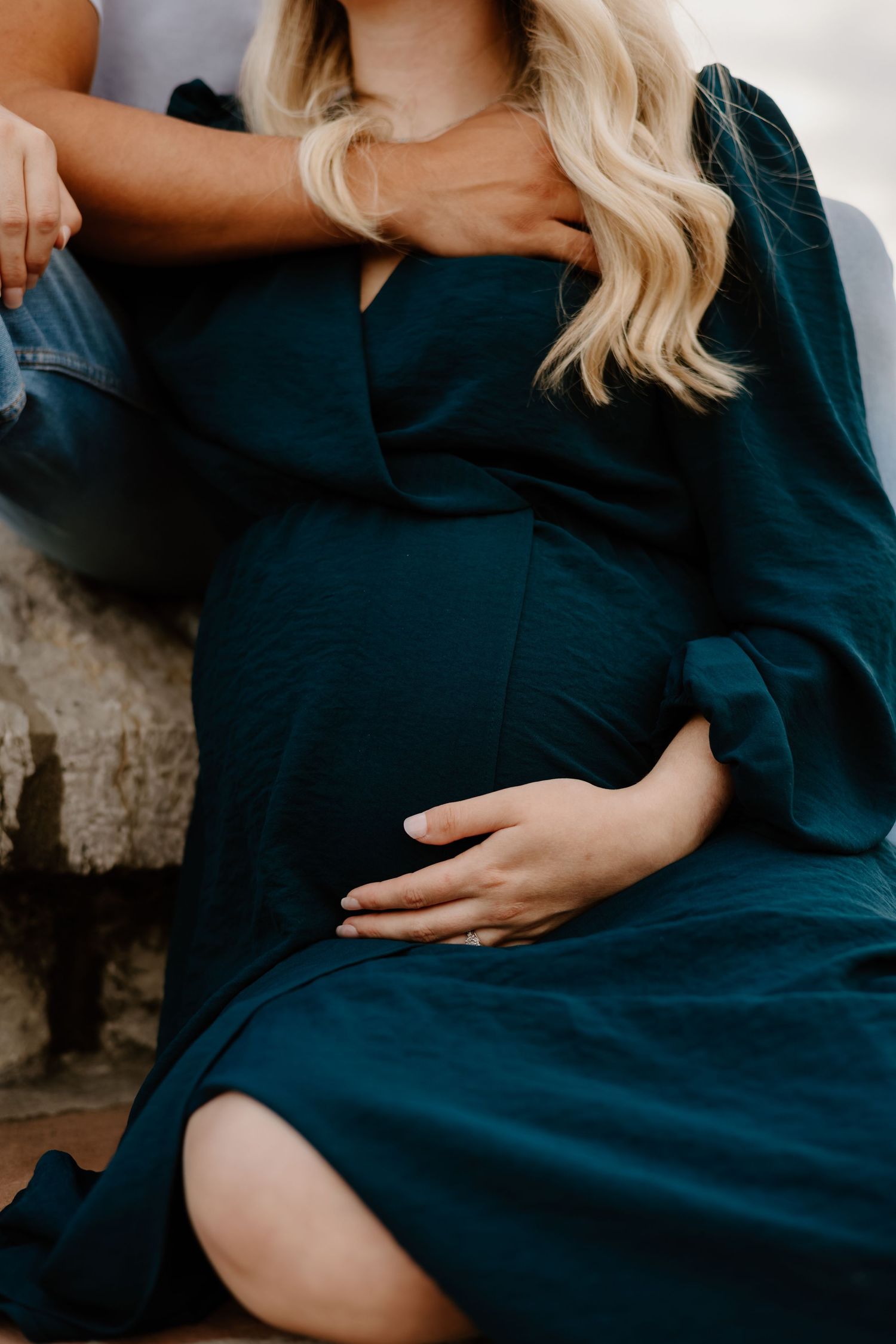 A pregnant woman in a navy blue dress sitting and cradling her baby bump.