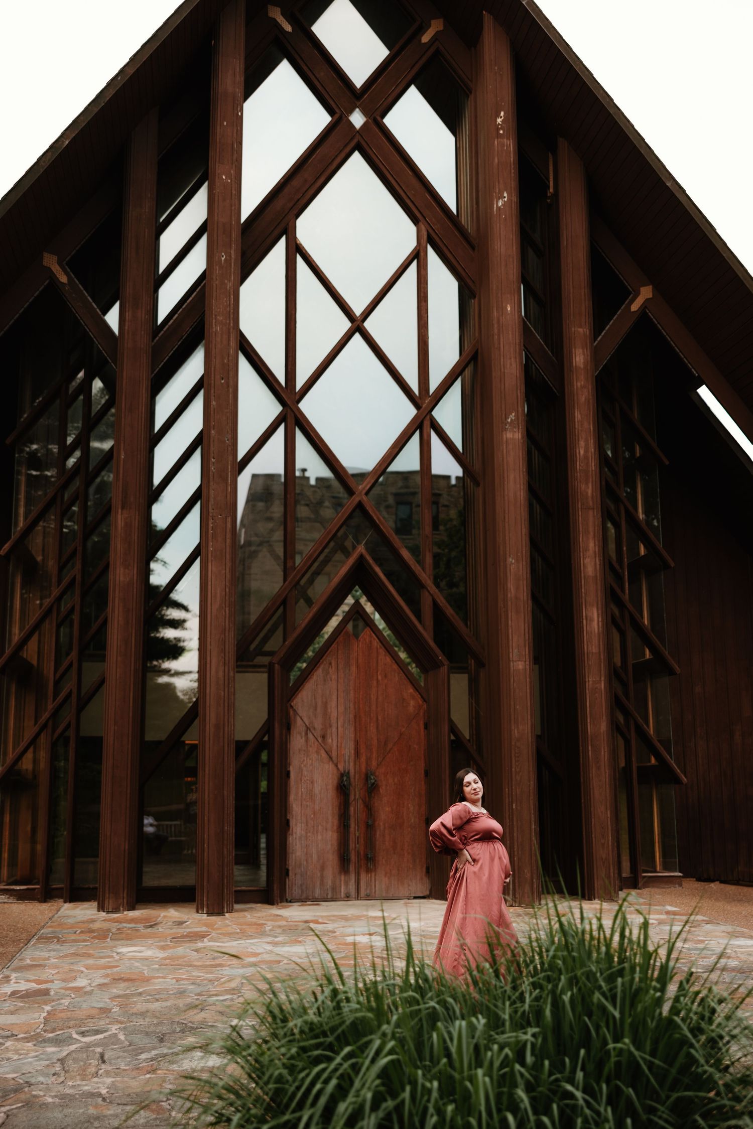 A person in a pink dress stands beneath dramatic wooden beams of a modern chapel.