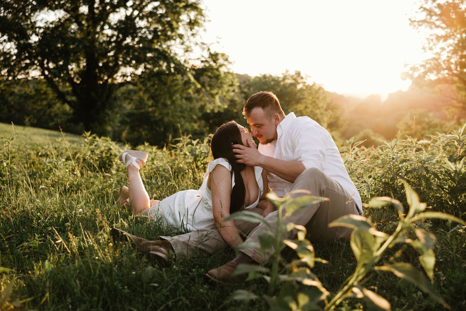 Intimate moment between couple laying in sunlit meadow during sunset.