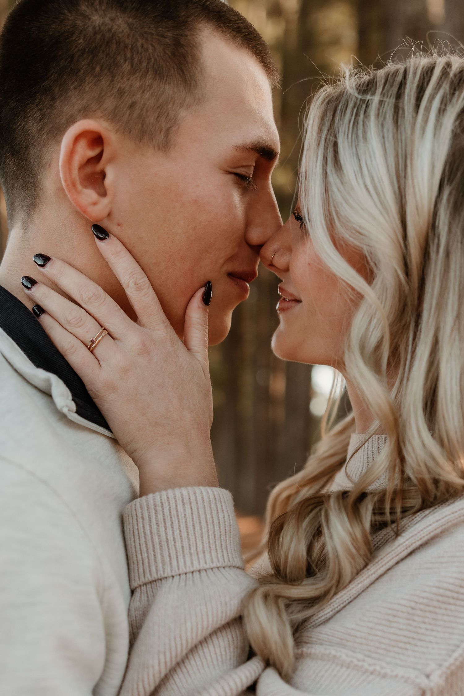 Close-up of a couple about to kiss outdoors, woman wearing a gold ring touching mans face tenderly.