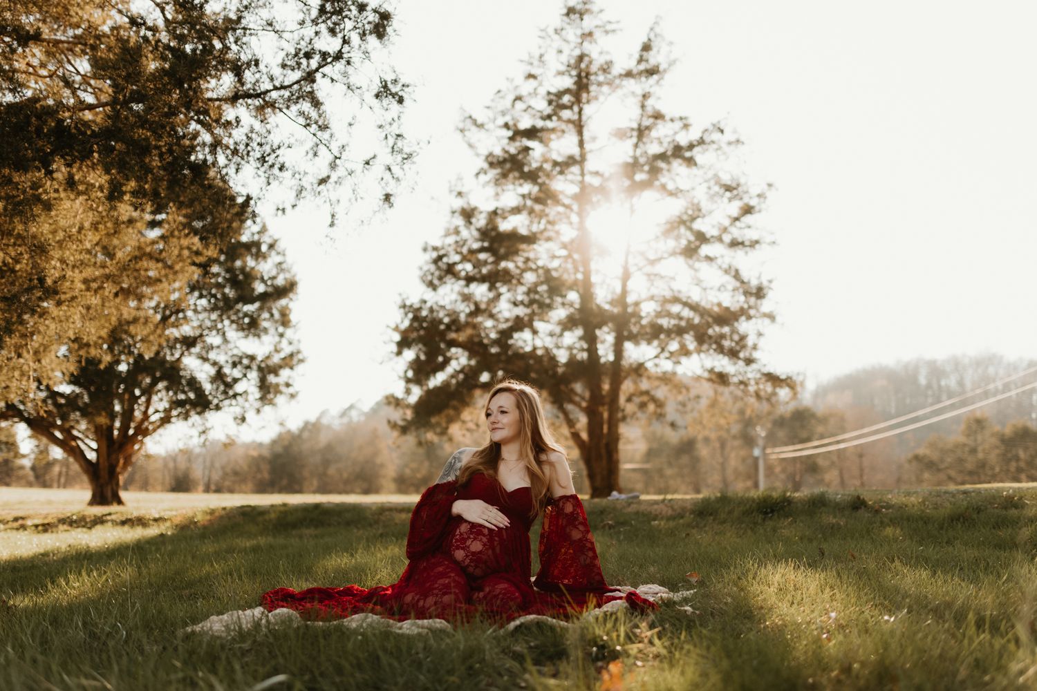 Silhouette of a person in a flowing dress against a warm sunset beneath tall trees.
