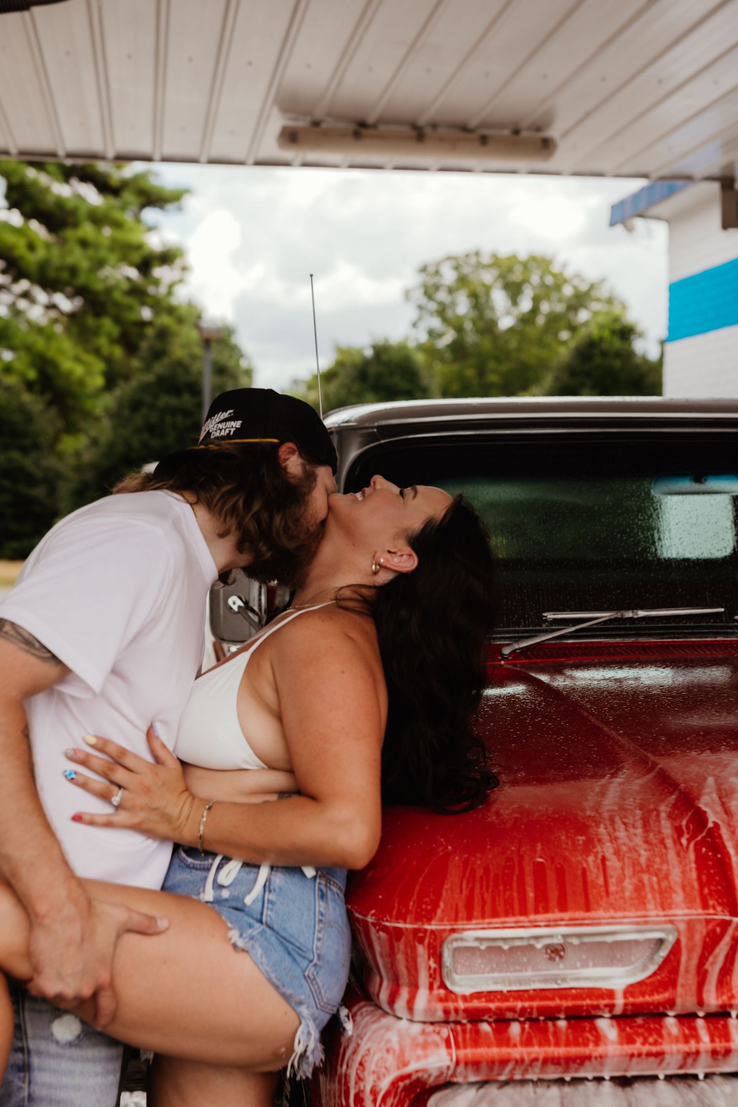 A passionate embrace against a classic red car at a car wash.