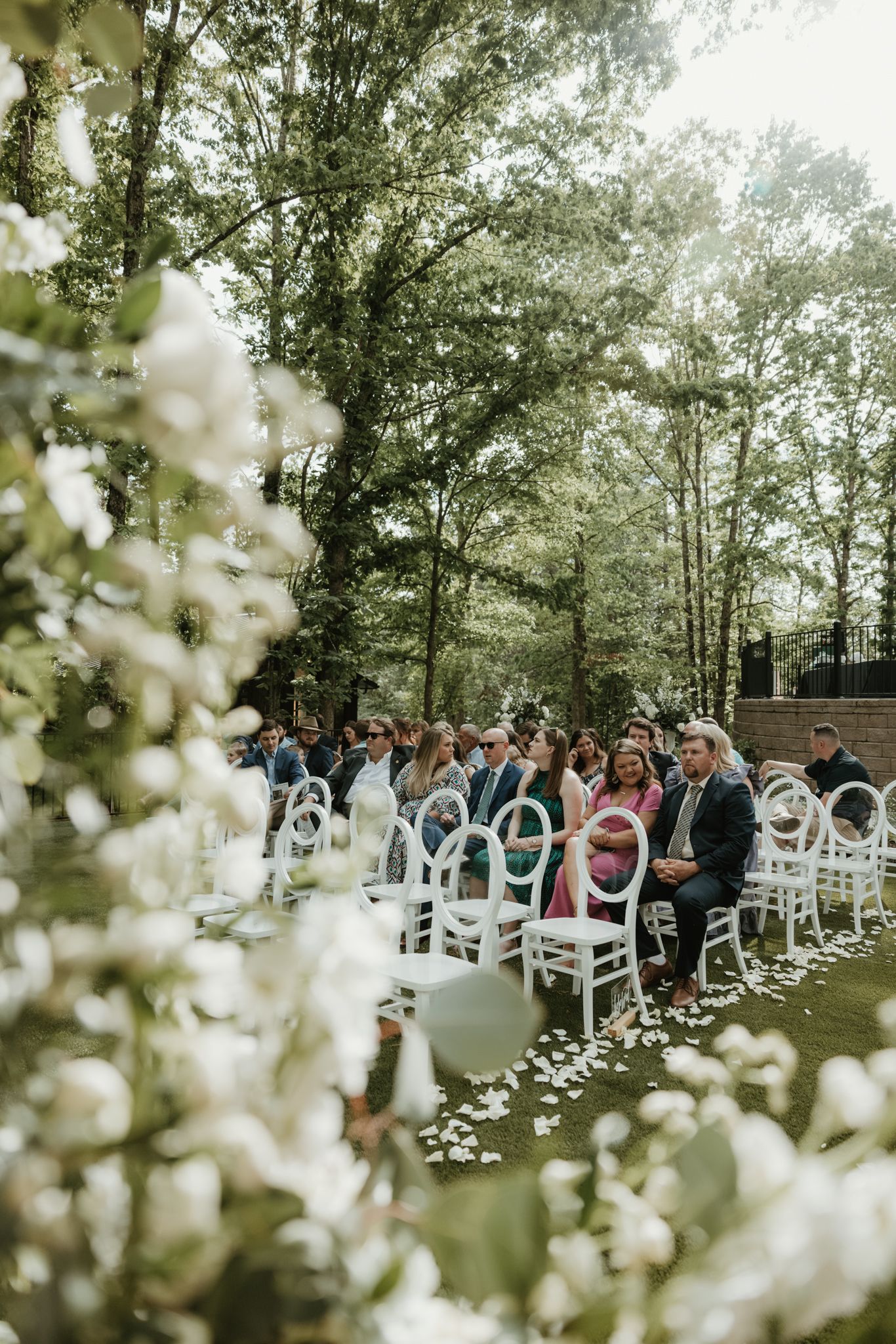 Outdoor wedding ceremony setting with white chairs and delicate floral decorations along a garden aisle.