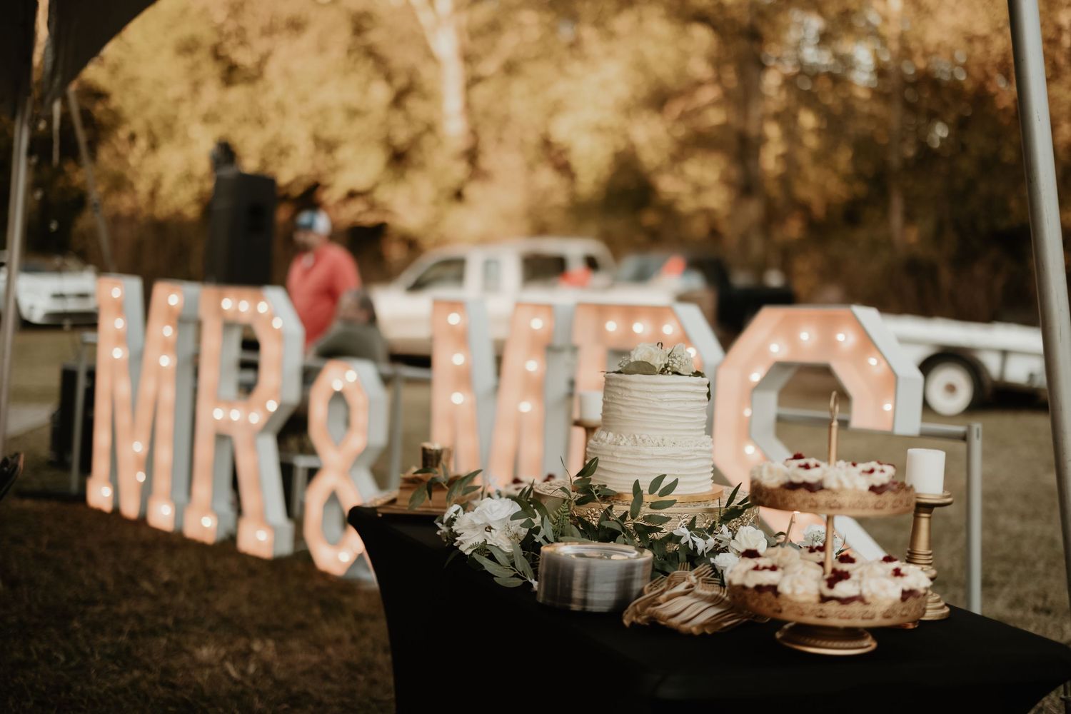 Wedding reception decor with large letters spelling 'Mr & Mrs' and rustic table settings at outdoor venue.