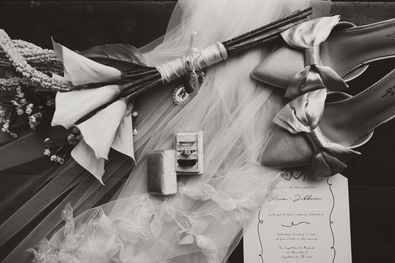 Black and white still life of wedding accessories including veils and invitation.