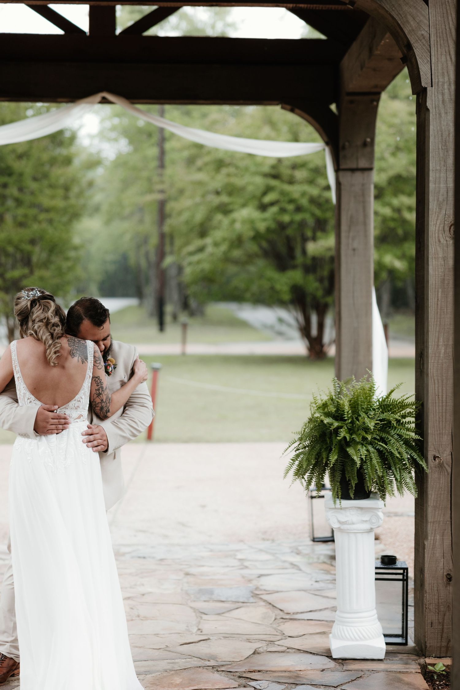 Wedding couple sharing a tender moment under a wooden pergola with hanging plants.
