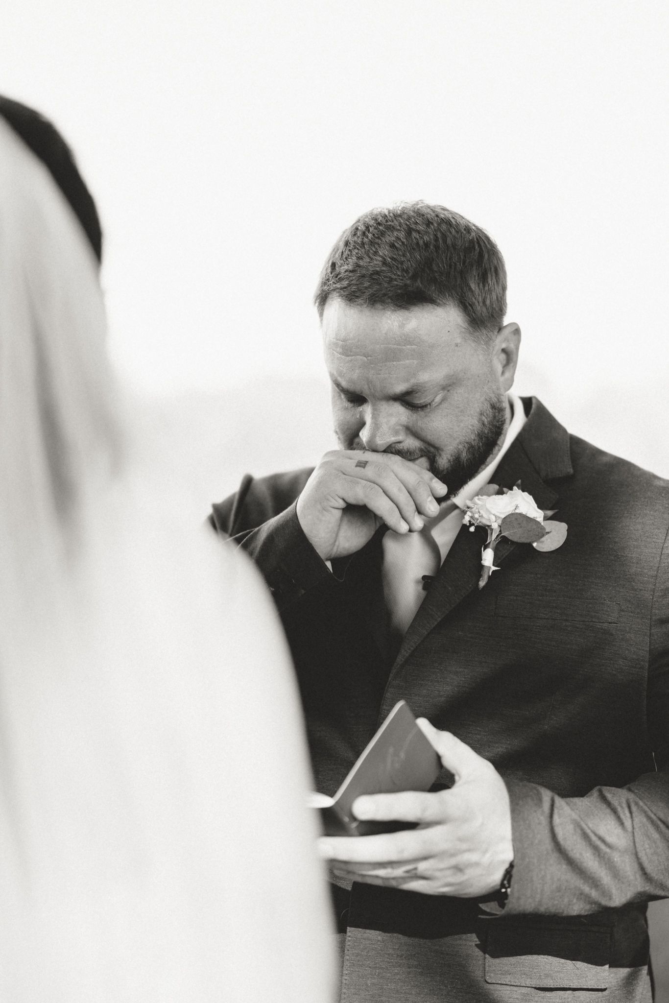 An emotional groom wipes away tears while reading a heartfelt letter on his wedding day.