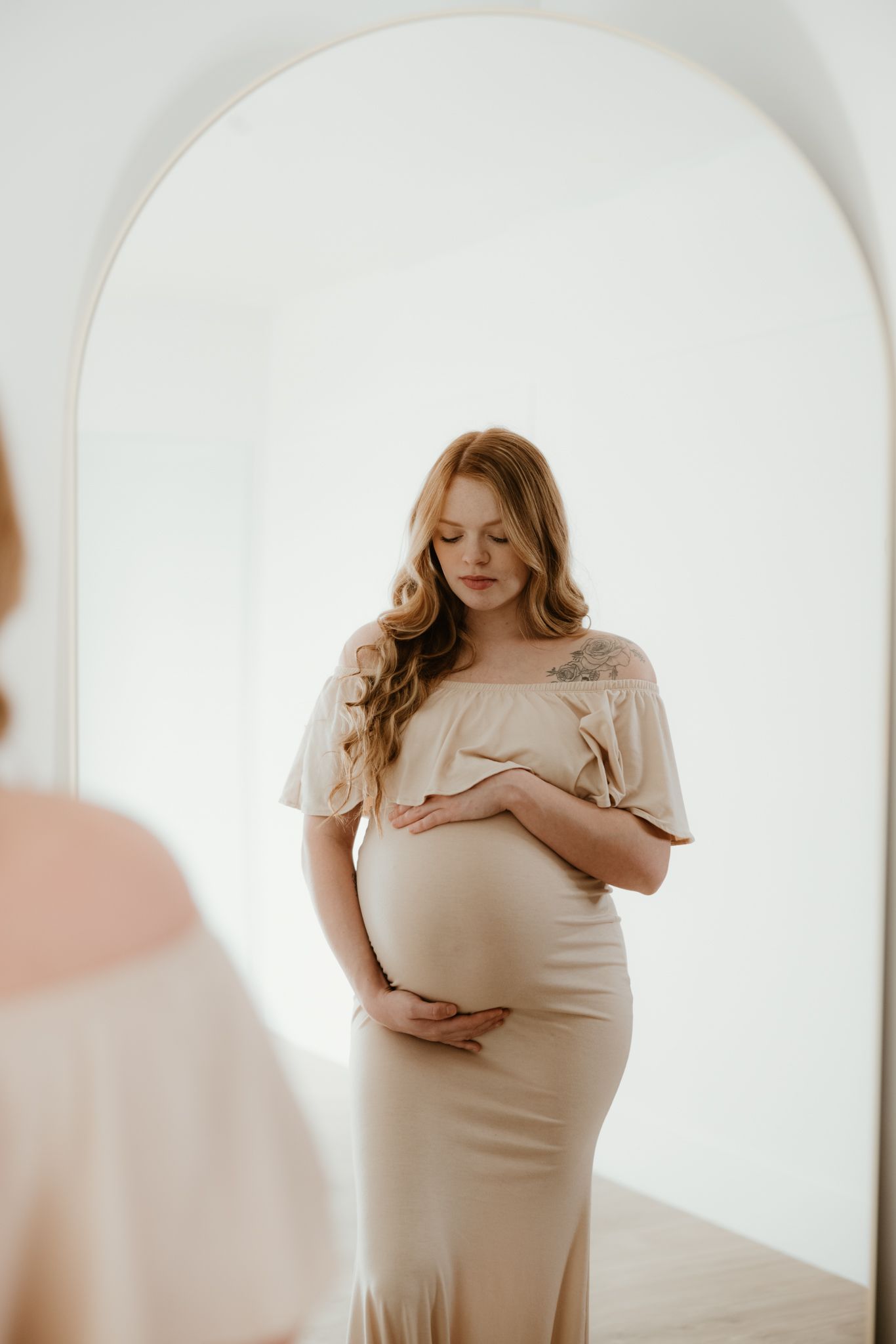 A person in beige dress stands in arched doorway of minimalist white room.