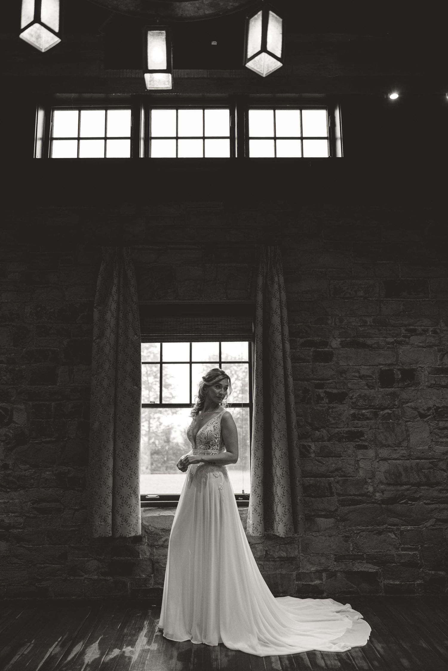 Dramatic black and white silhouette of a bride standing by window in a flowing gown.