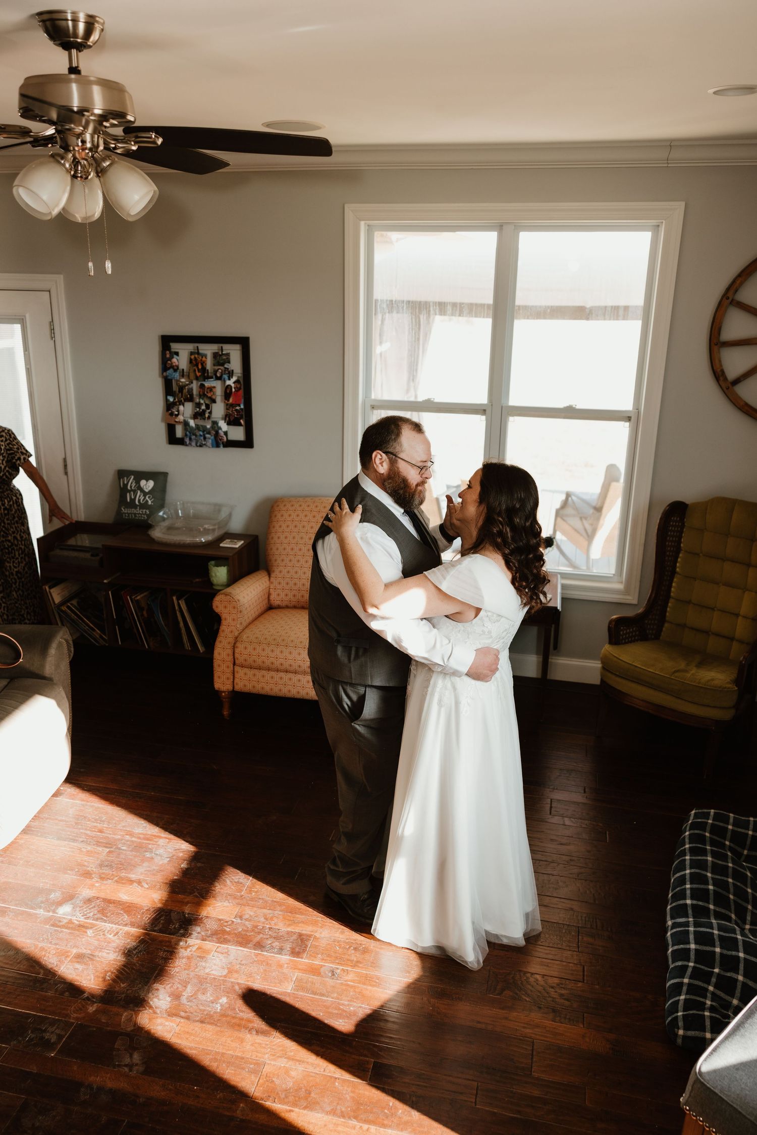 A bride and groom share a romantic dance in a warmly lit living room with hardwood floors and vintage furniture.