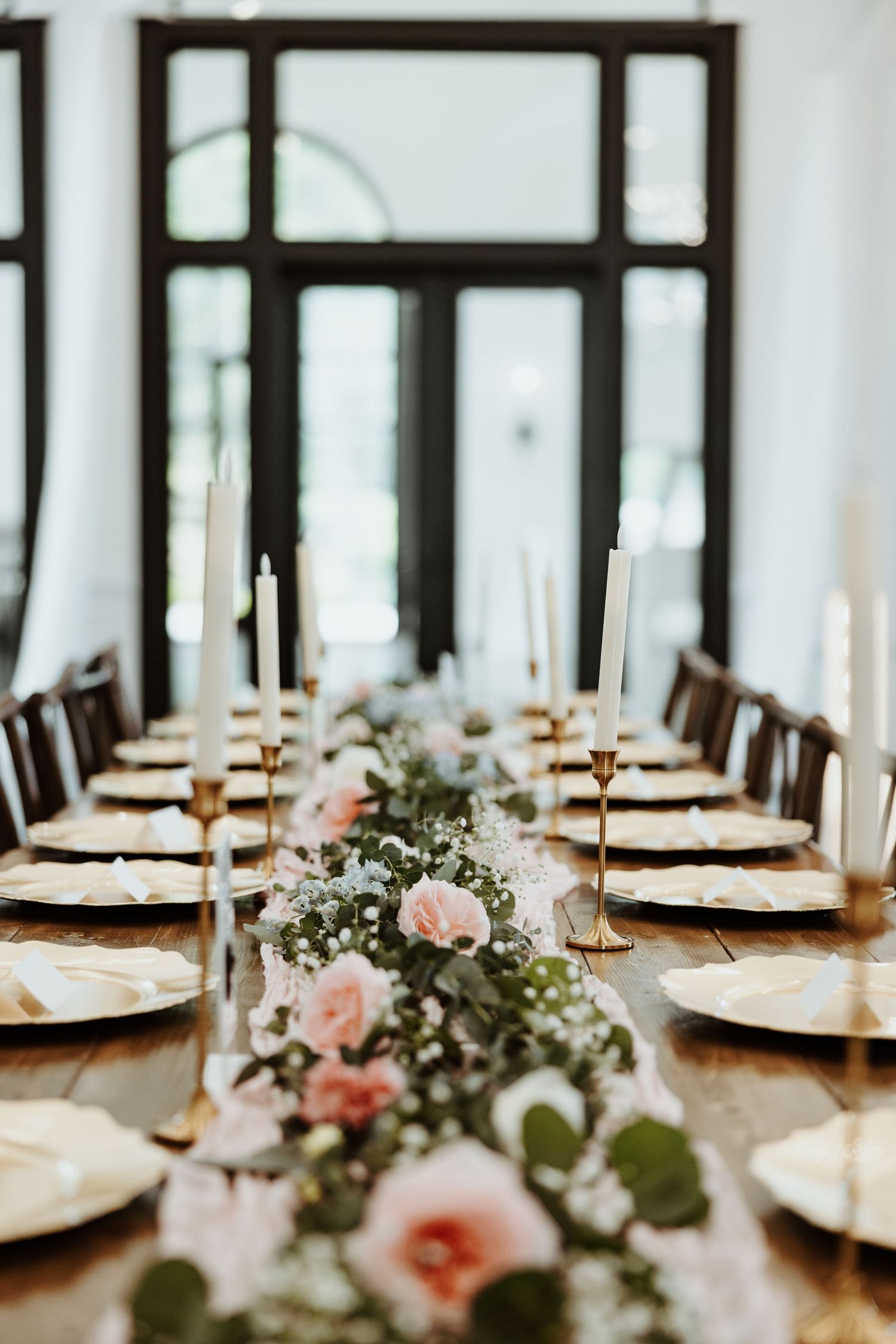 Elegant wedding reception table with gold chargers, white taper candles, and pink floral greenery runner centerpiece.