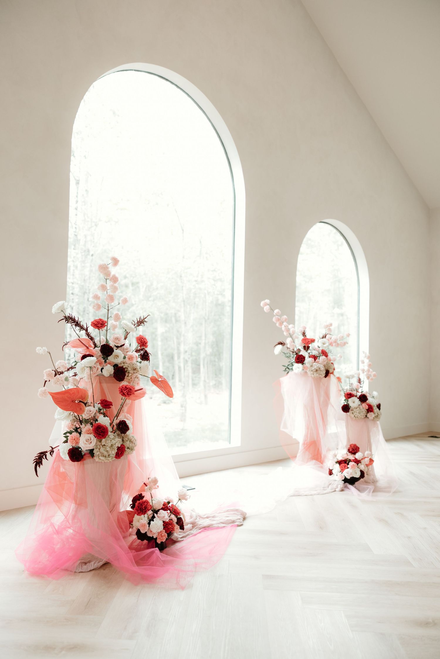 White wedding chapel decorated with pink and white floral arrangements near arched windows.