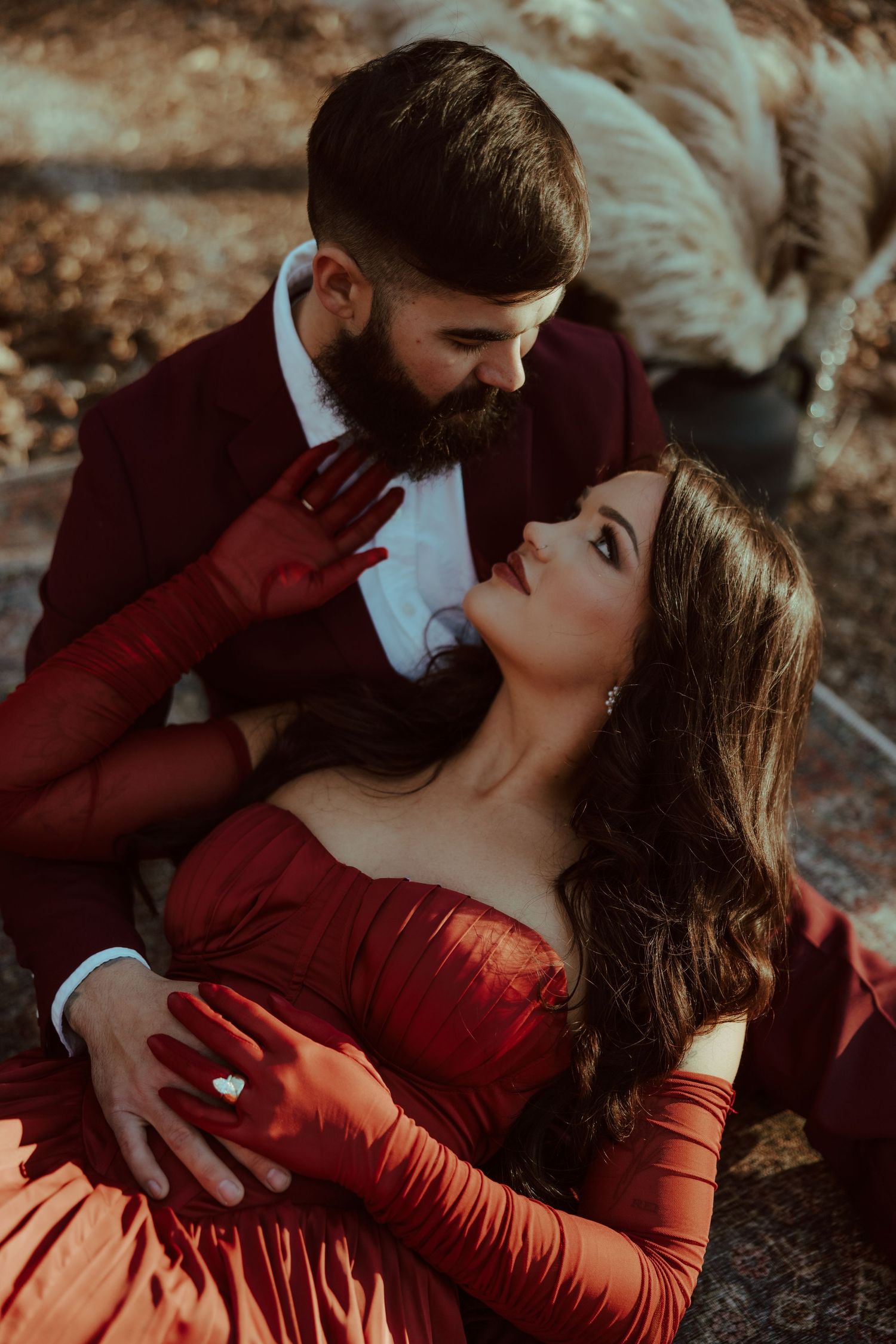 A couple in matching red outfits share a romantic moment outdoors, with the woman reclining against the bearded man.