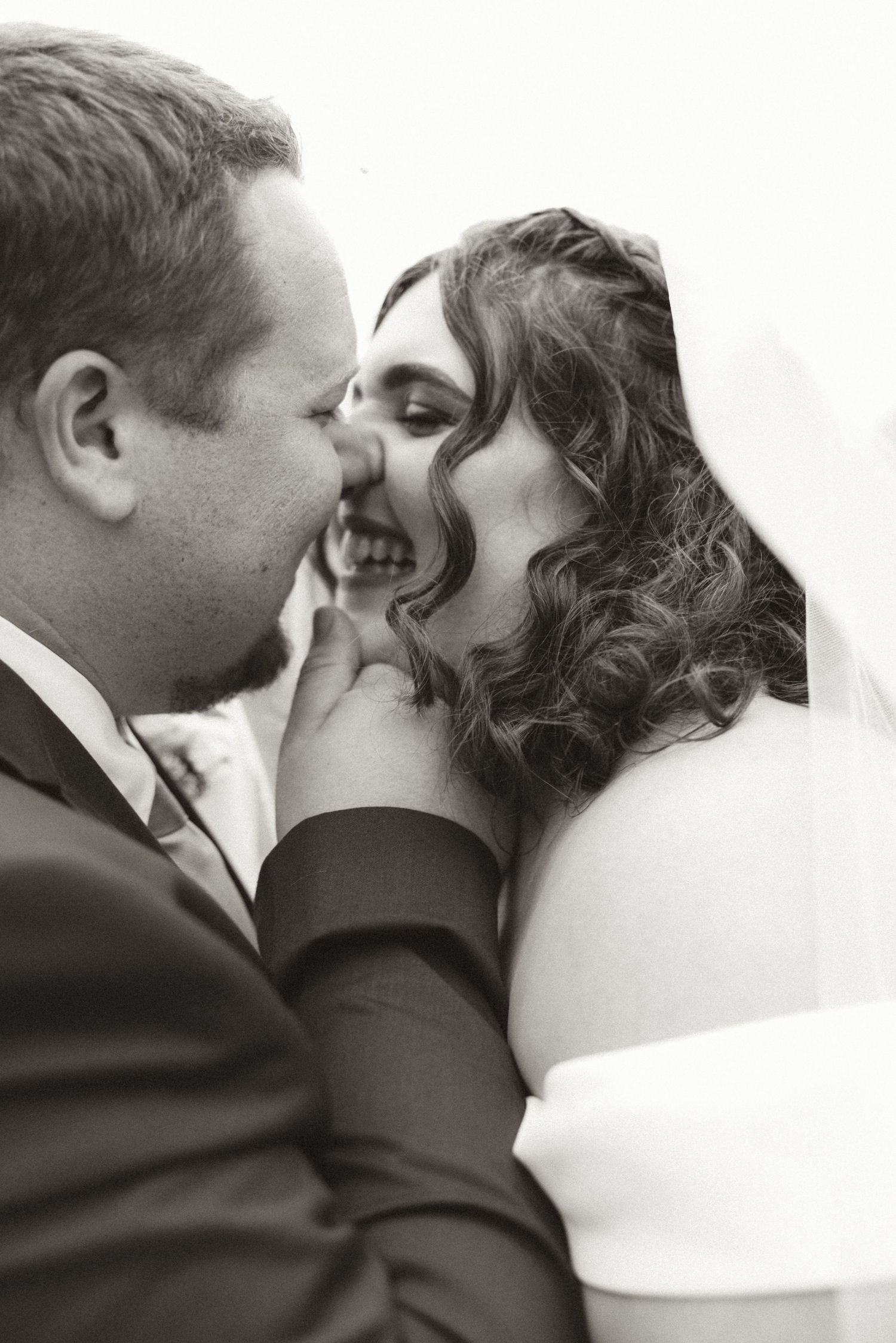 Intimate black and white wedding photo showing tender emotional moment between newlyweds in formal attire.