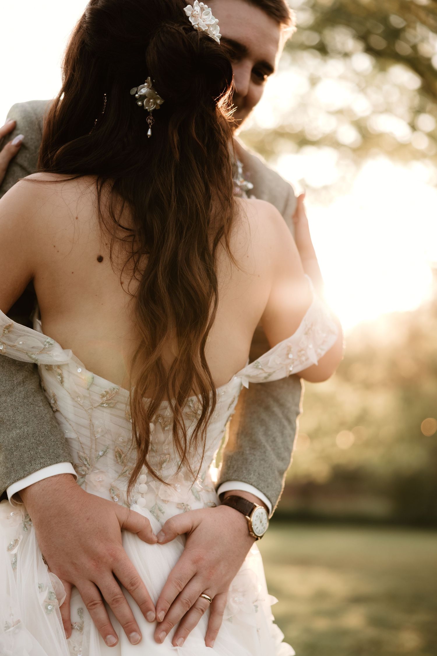 A romantic sunset moment at a wedding with a lace dress and gentle embrace forming a heart shape with hands.