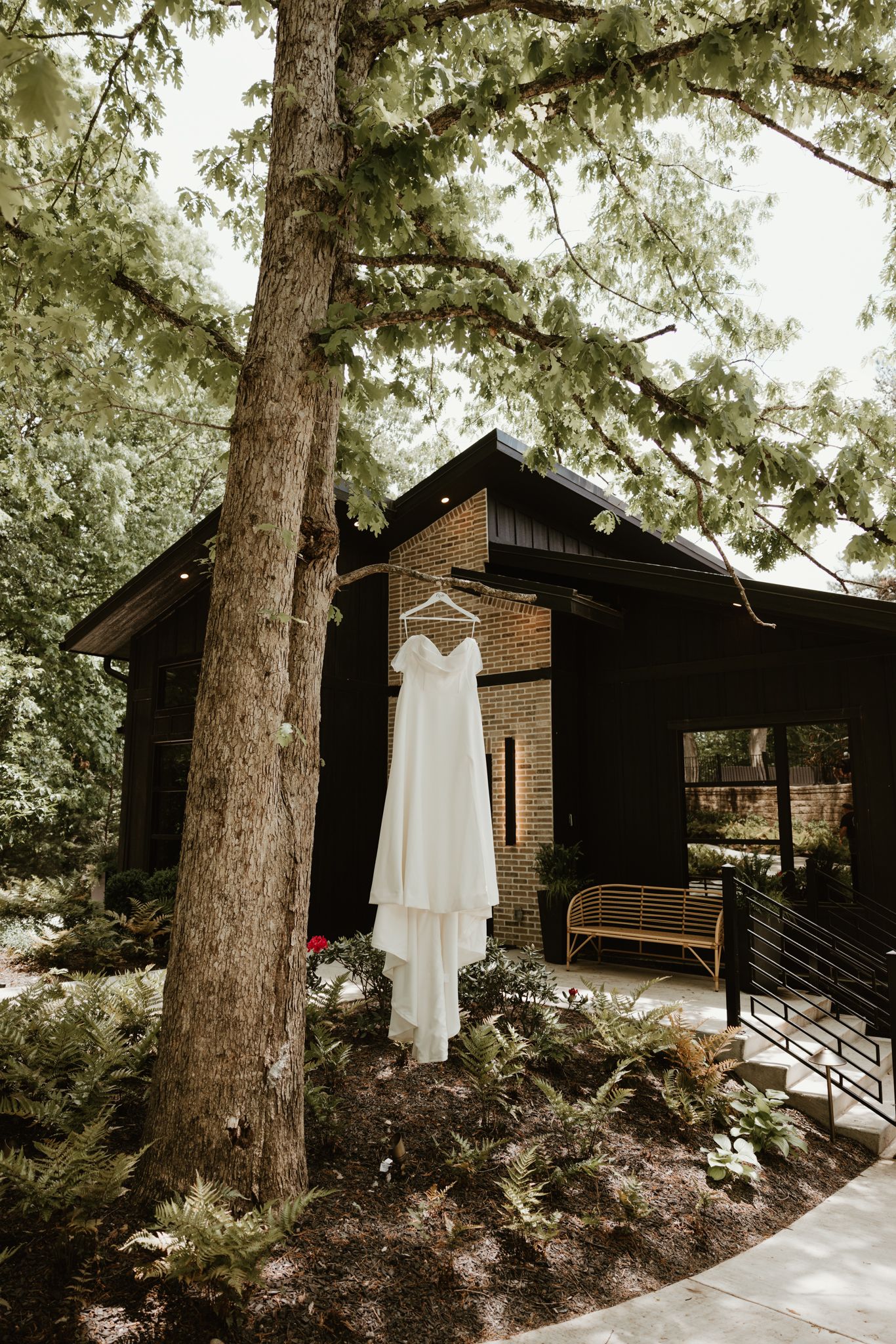 A white wedding dress hangs outside a modern black cabin surrounded by tall evergreen trees.