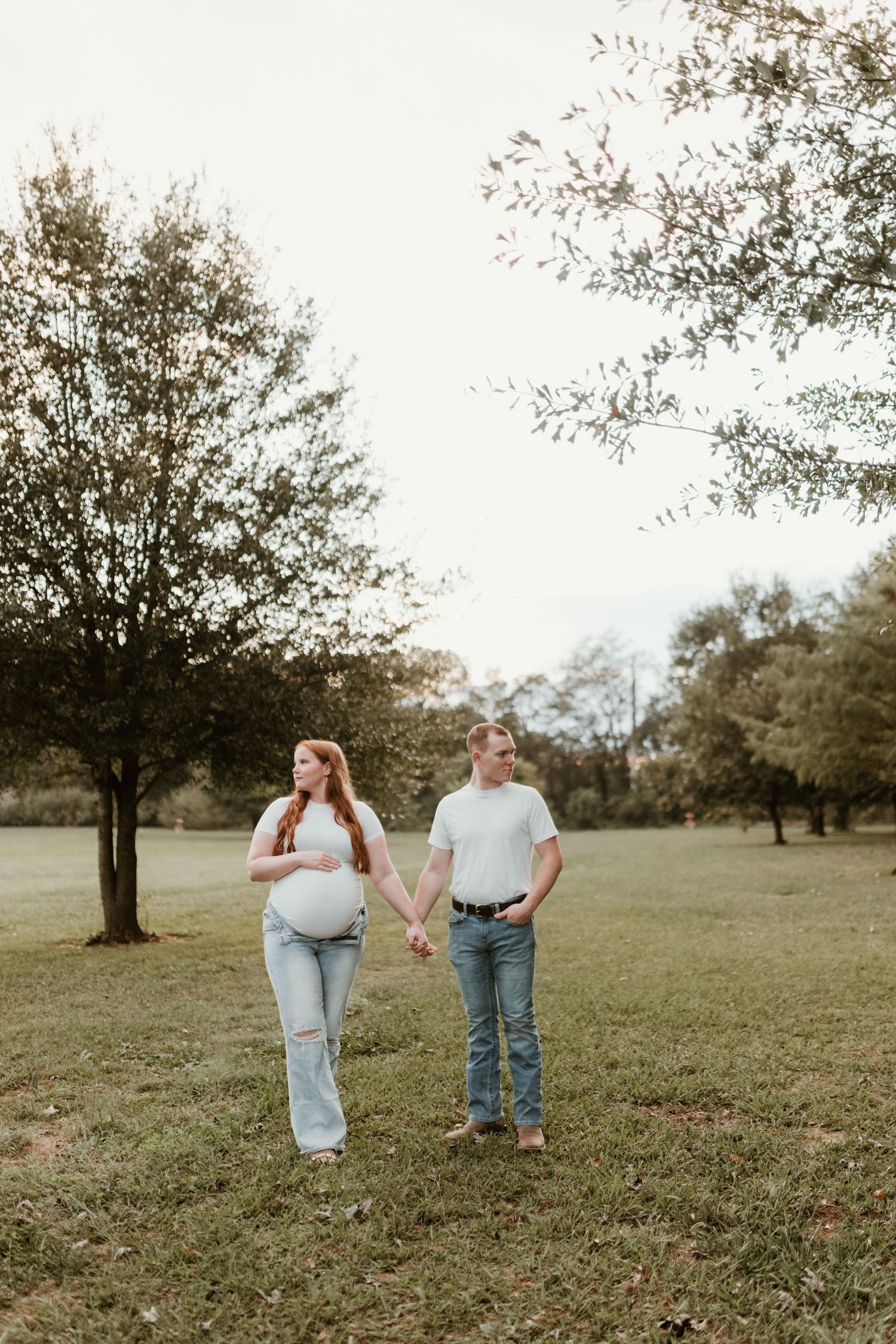A couple walking together while holding hands in an open grassy field during a sunny autumn day.