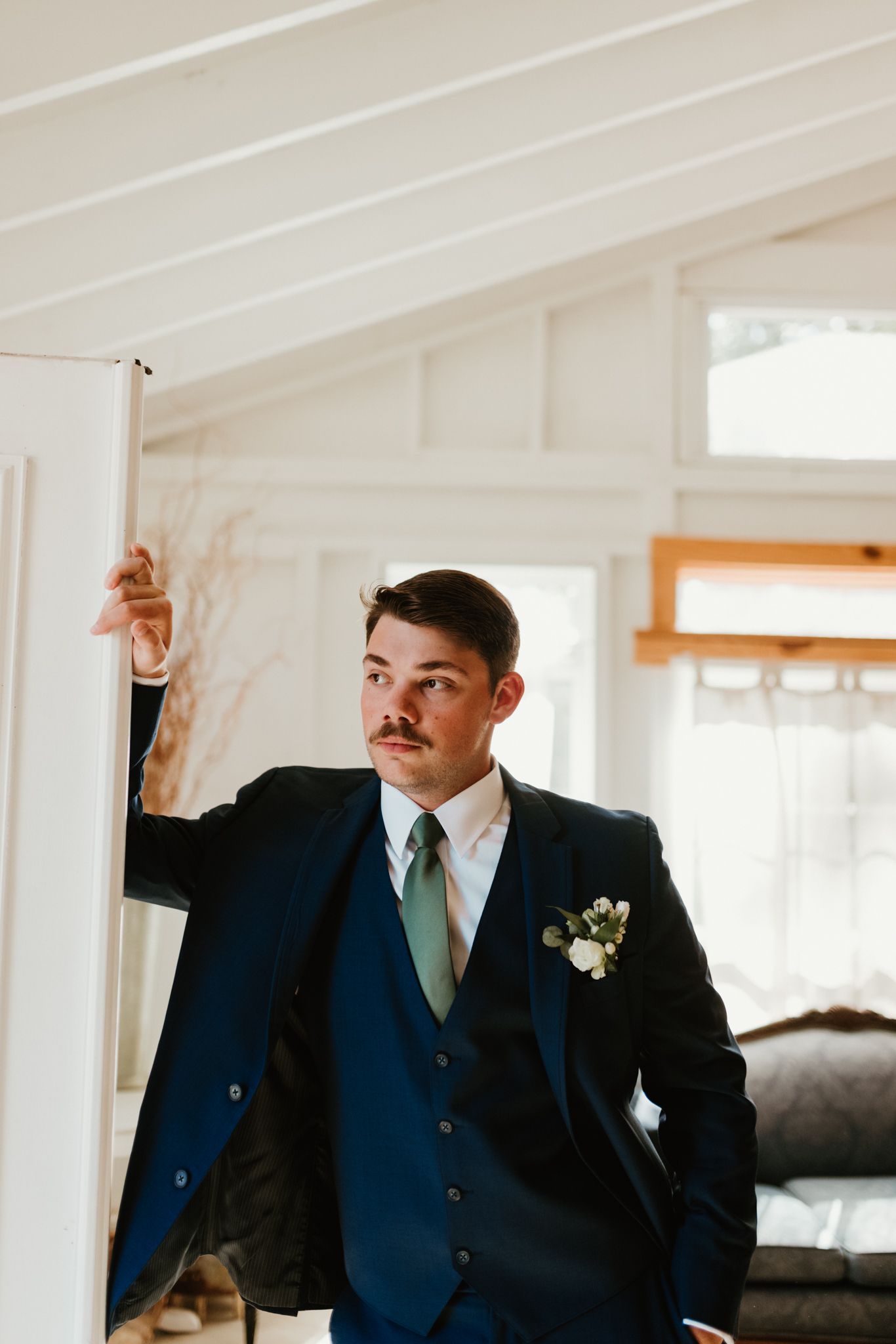 A groom in a navy suit poses in a bright indoor setting with natural light.