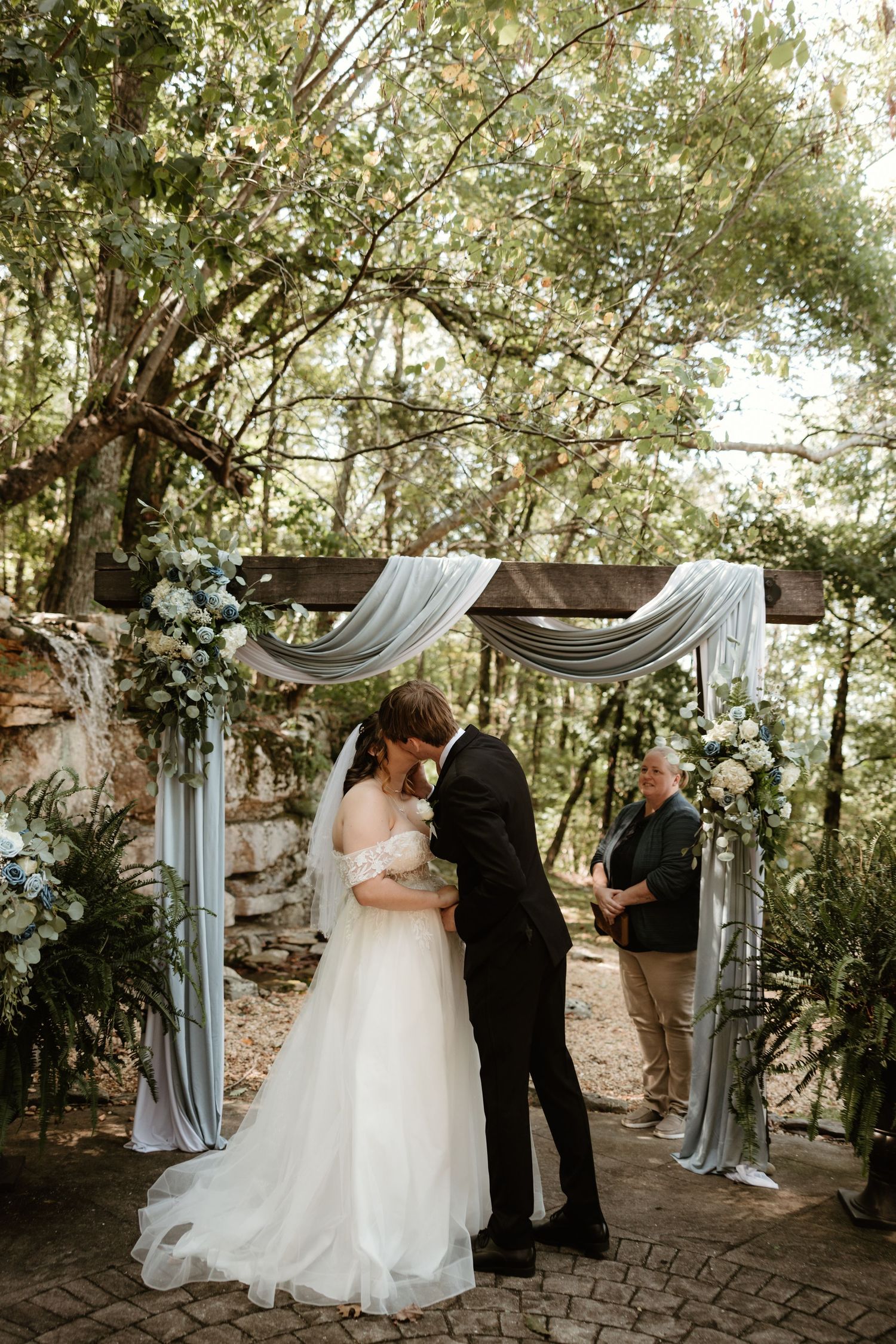 Wedding ceremony setup with draped fabric arch in a rustic outdoor garden setting during daytime.