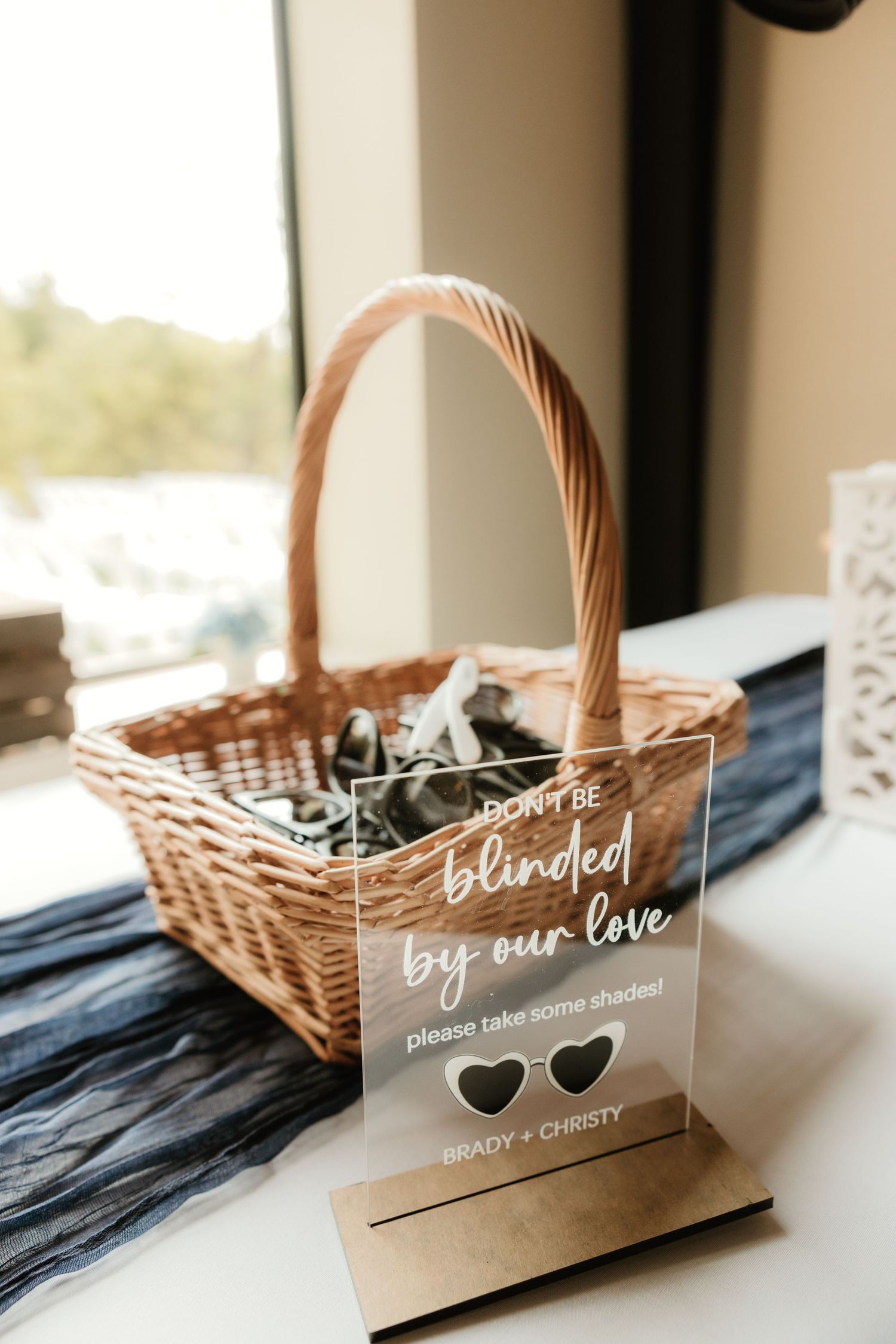 Wicker gift basket with delicate white lace trim and calligraphic signage displayed at wedding favor station.