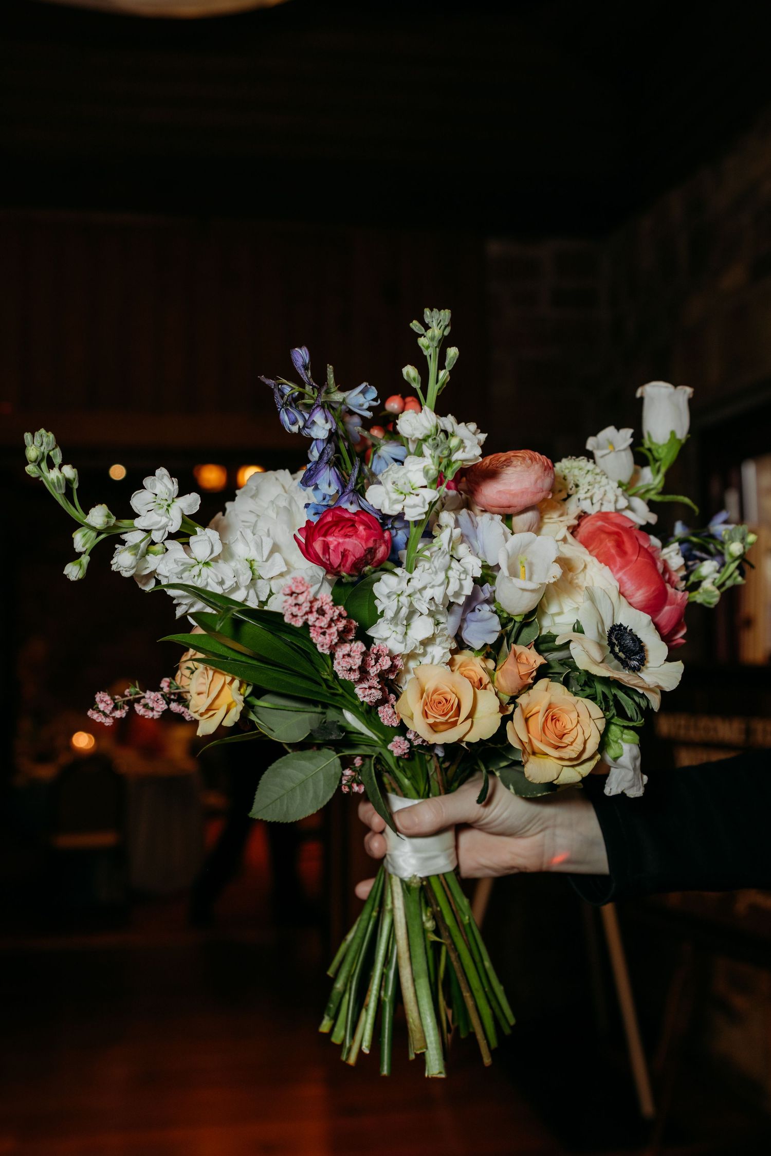 Colorful wedding bouquet with roses, peonies and mixed flowers against a dark background.