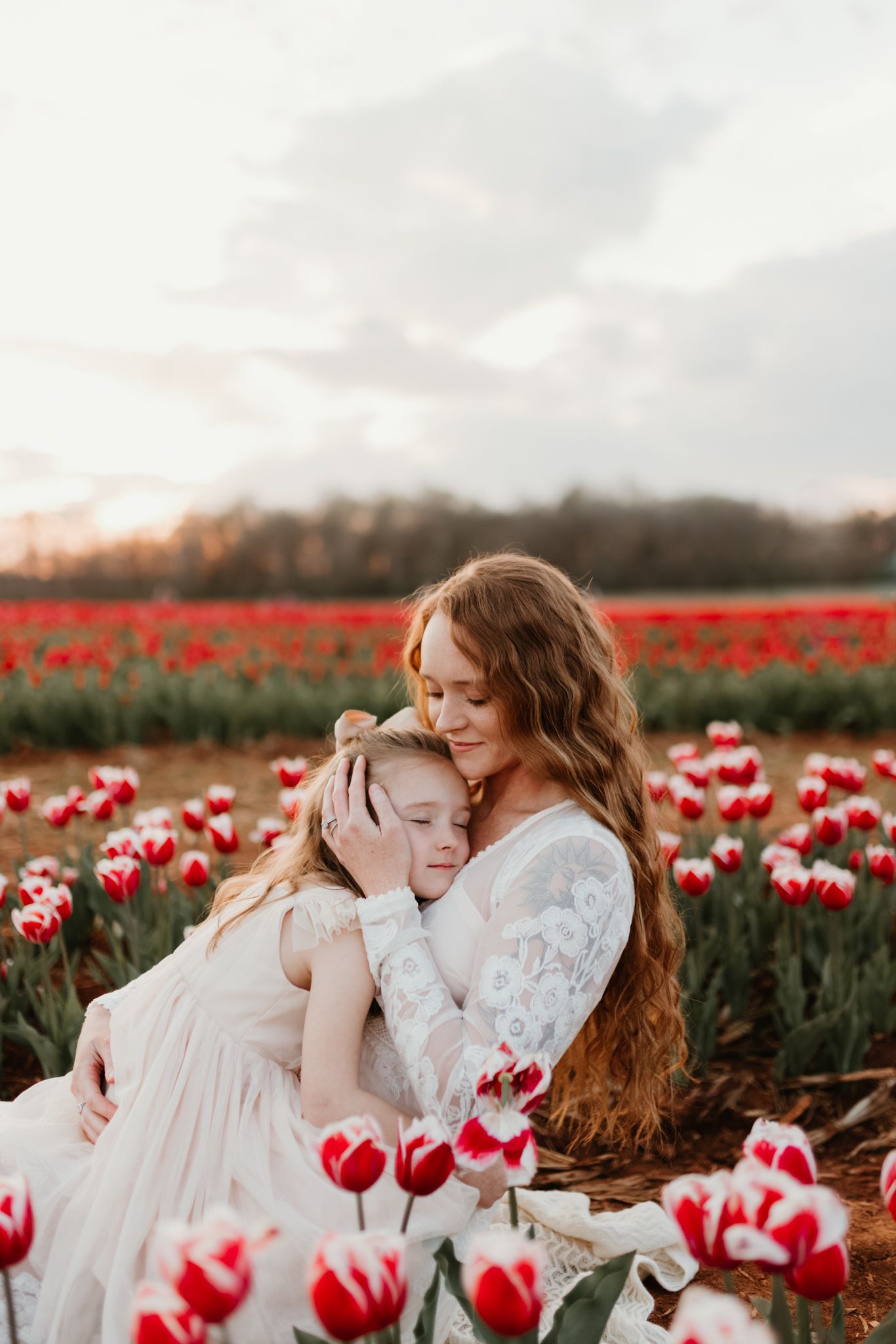 Two figures share a tender moment in a stunning field of red and white tulips at sunset.