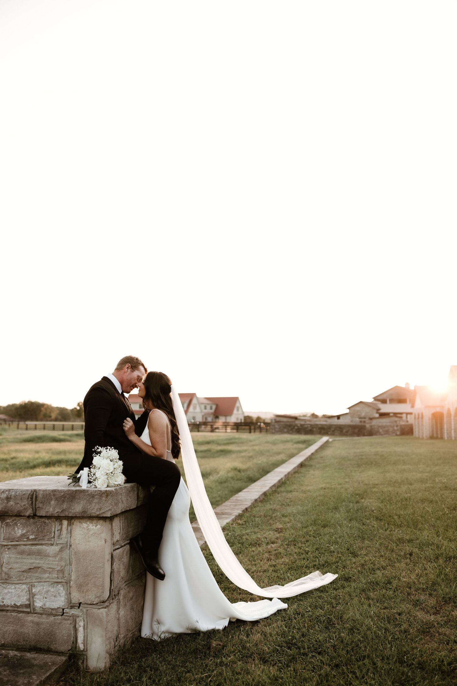 Wedding couple shares intimate moments along stone wall at sunset in countryside setting.
