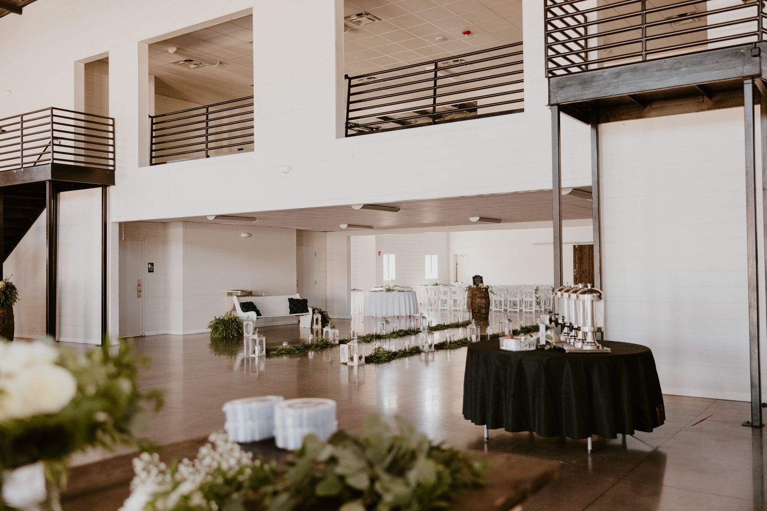 Modern event venue interior with white walls, balconies and catering setup with black tablecloth and tables.