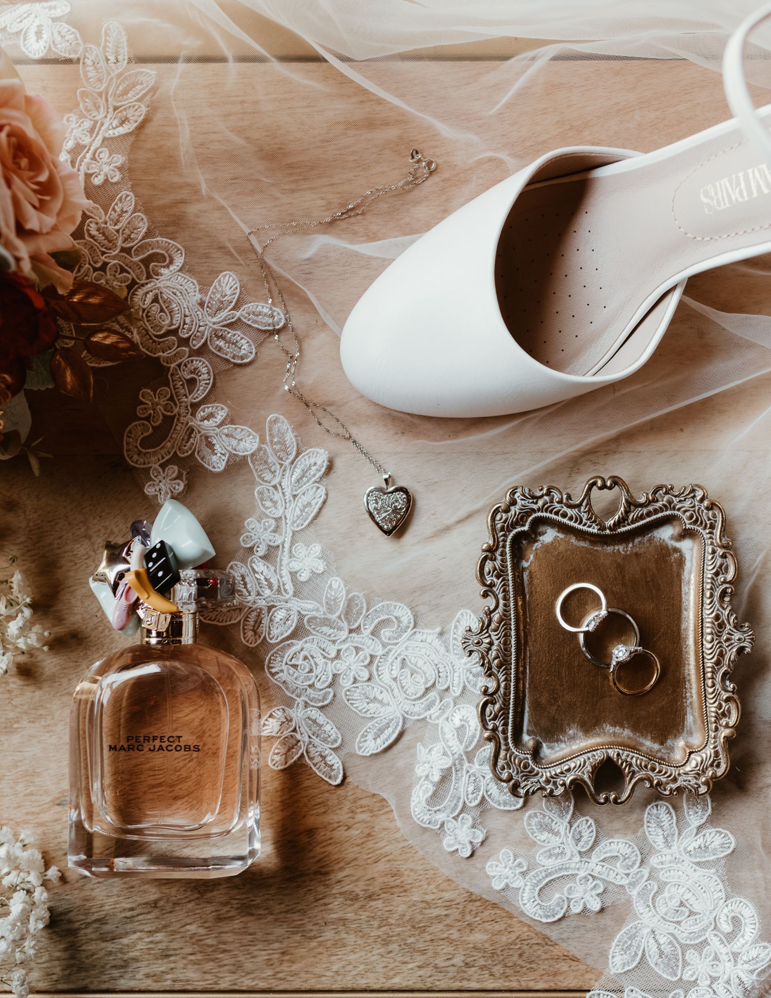 Wedding detail flatlay with white lace veil, shoes, perfume bottle and vintage tray holding rings.