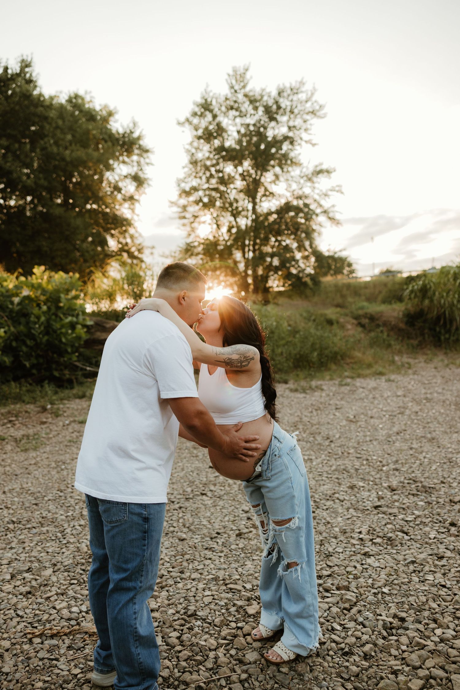 A romantic sunset moment between two people sharing a tender kiss on a rocky path amidst nature.
