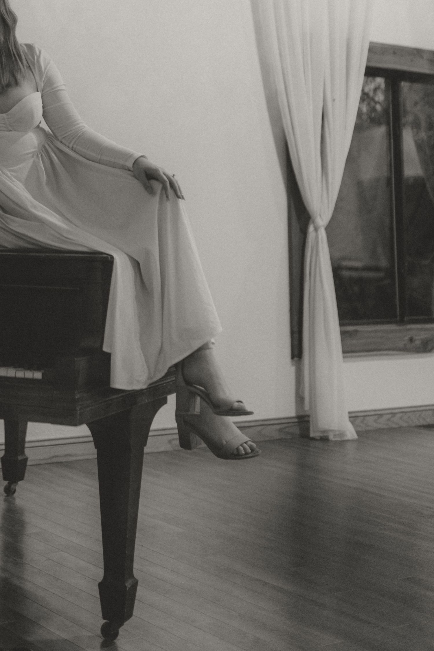 Black and white photo of elegant dress detail with figure seated at vintage piano.