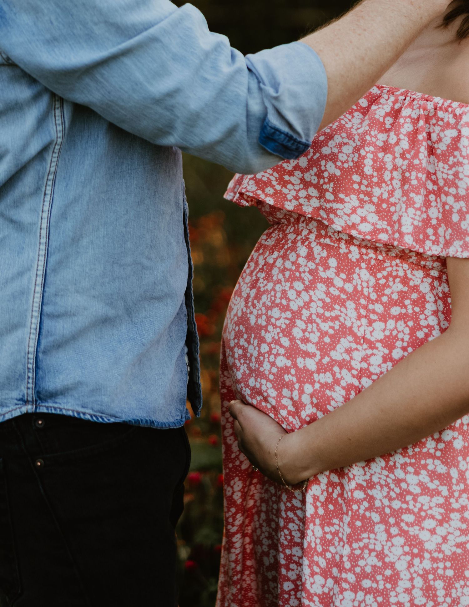 Close-up view of a couple in denim and floral dress showing a baby bump.