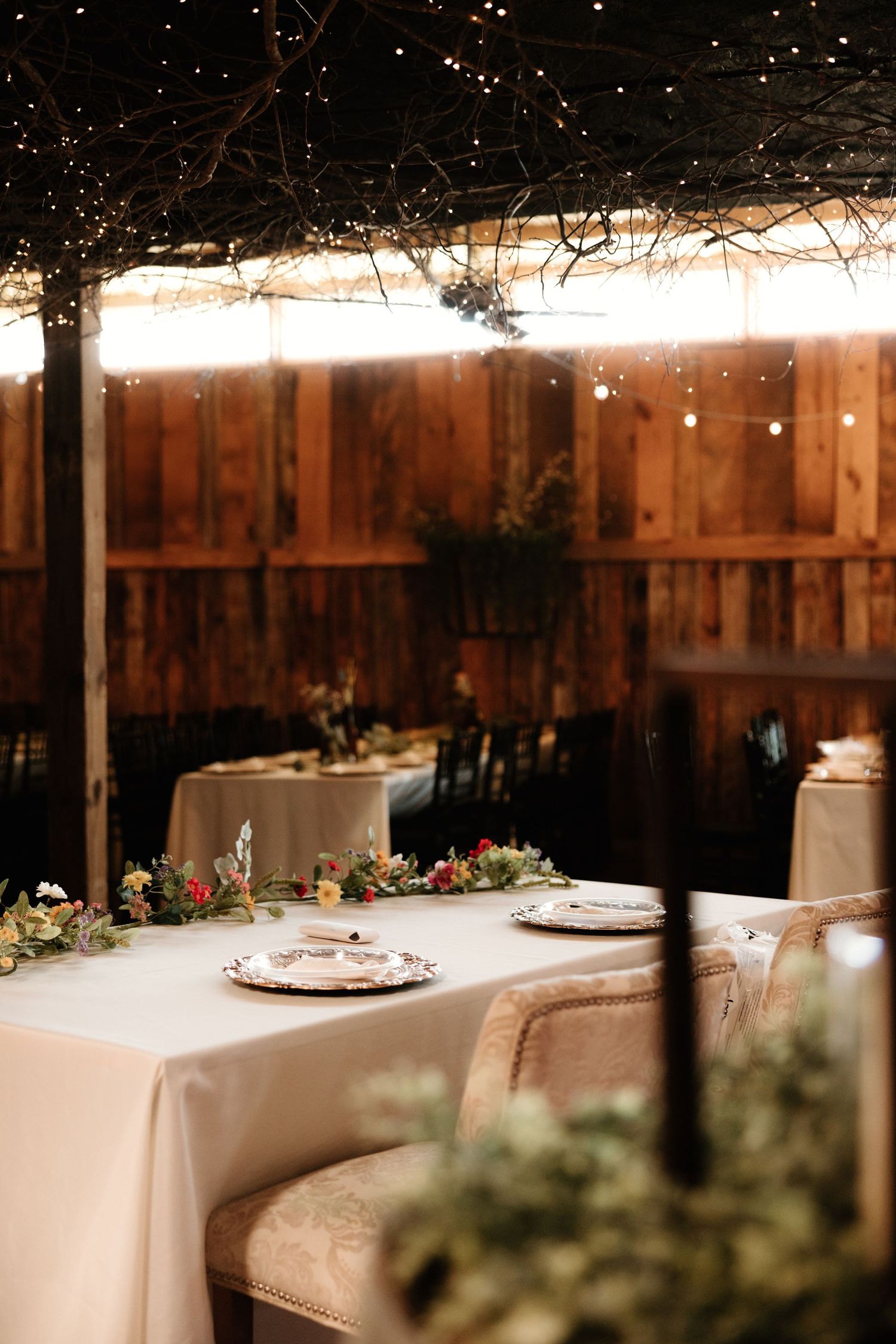 Rustic barn wedding reception setup with white tablecloths and string lights creating a romantic atmosphere.