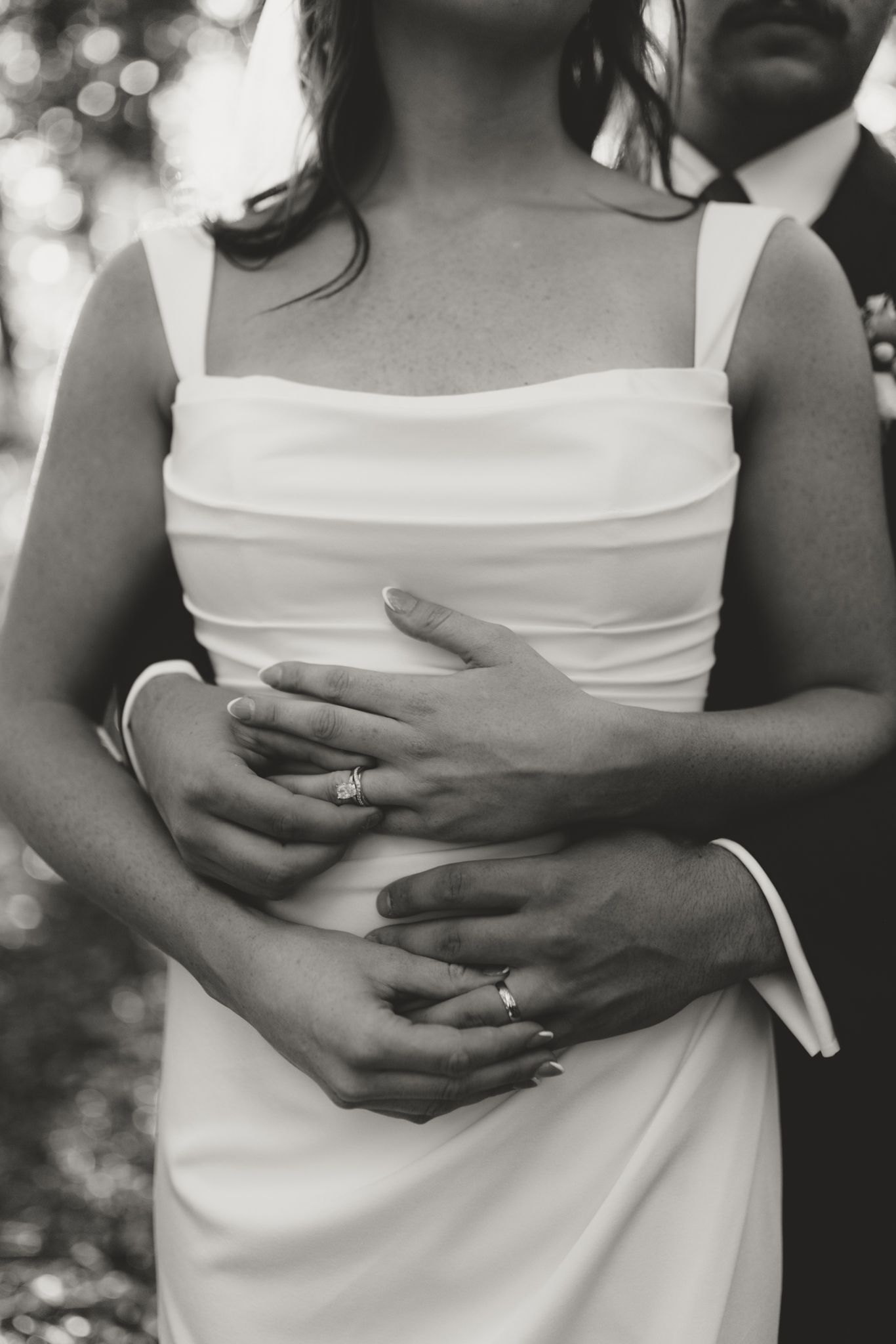 Close-up of hands embracing against a white wedding dress, showing an engagement ring.