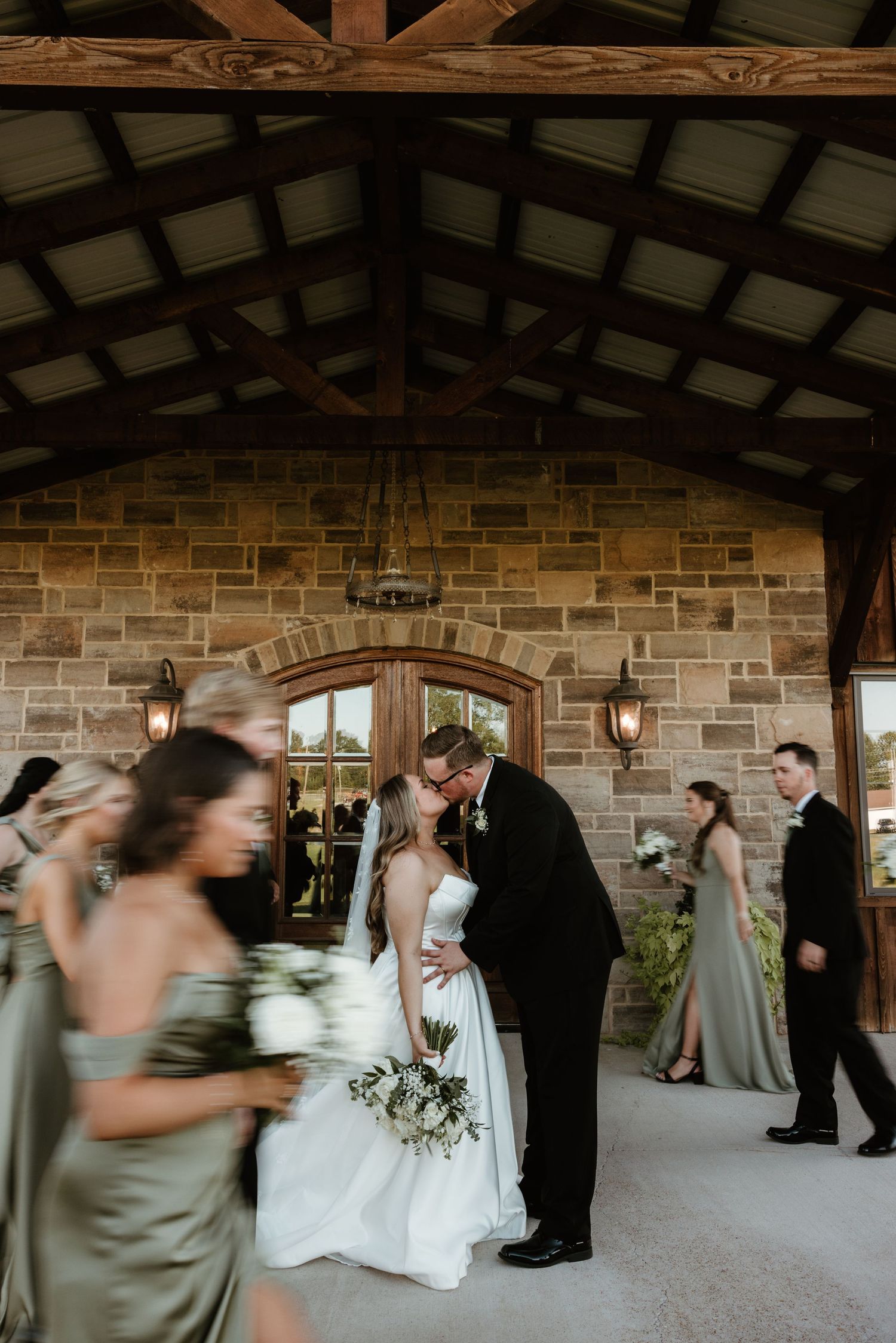 Motion blurred wedding party dancing in a rustic stone barn venue with wooden beams overhead.