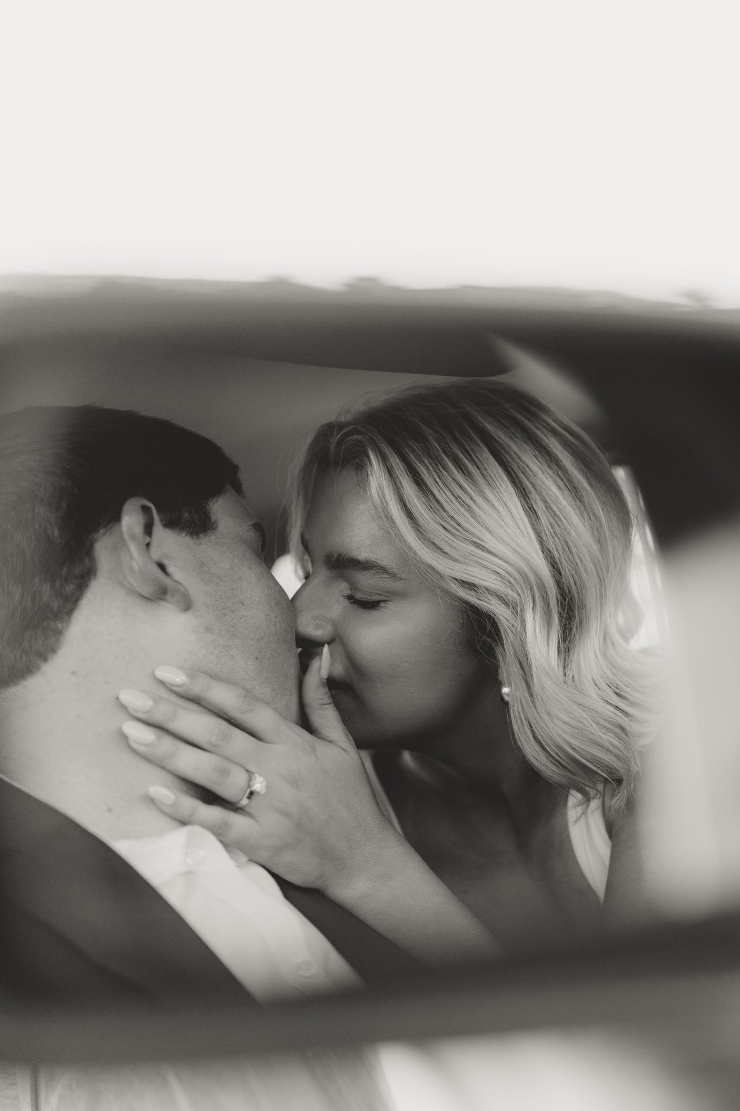 A romantic black and white portrait of a tender kiss between two people, with the woman's hand gently touching his face.