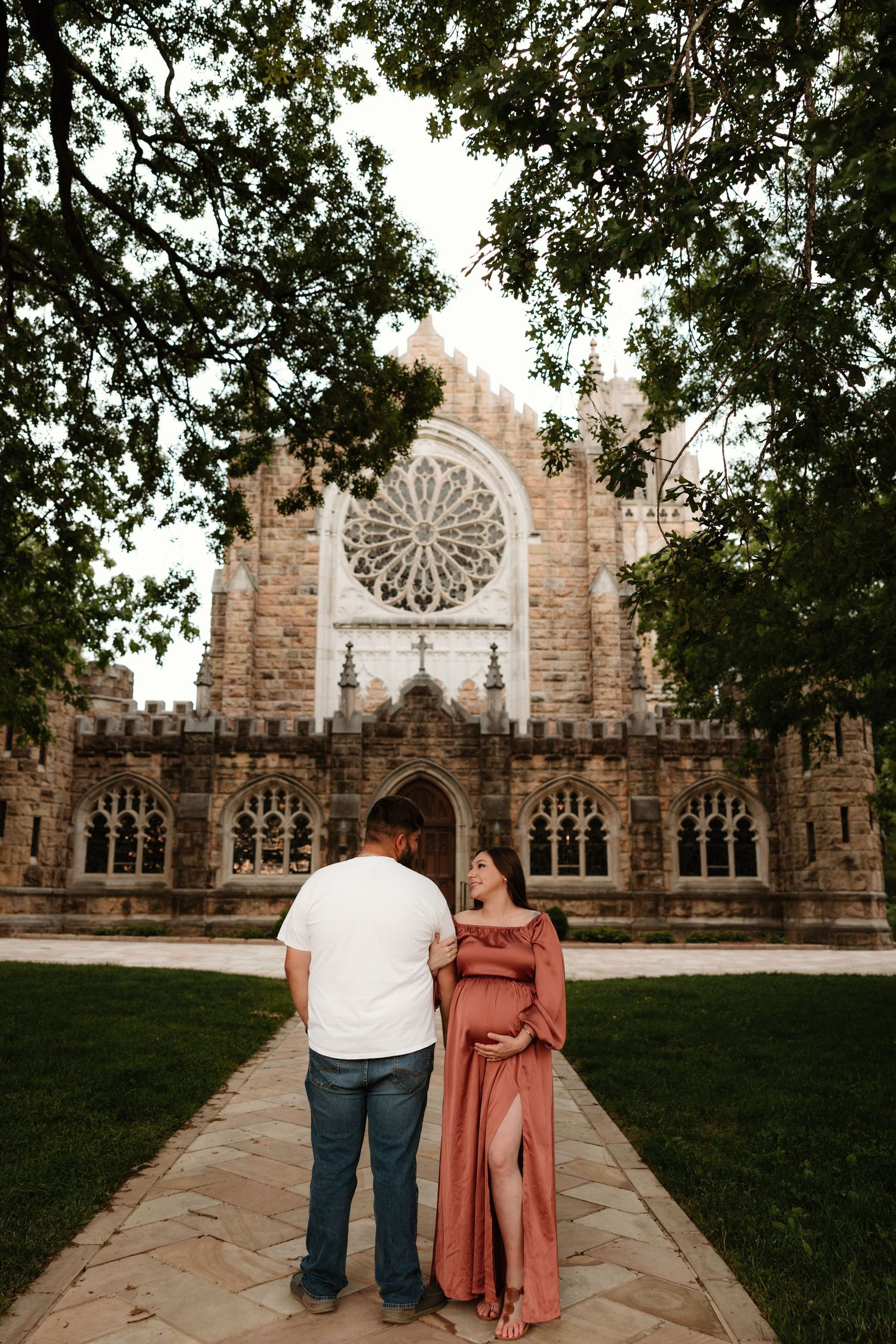 A couple stands before a historic church with a large rose window and gothic architecture.