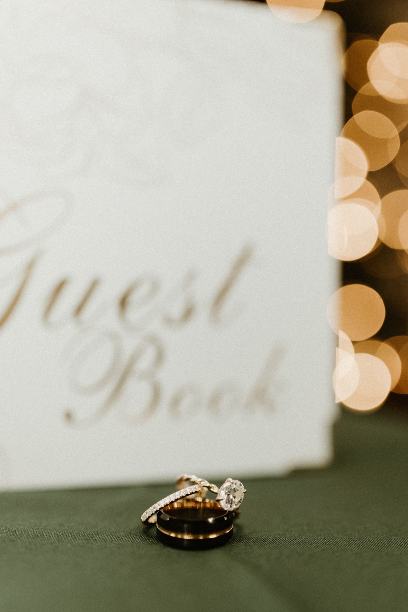 Wedding rings photographed with bokeh lights and guest book in soft focus.