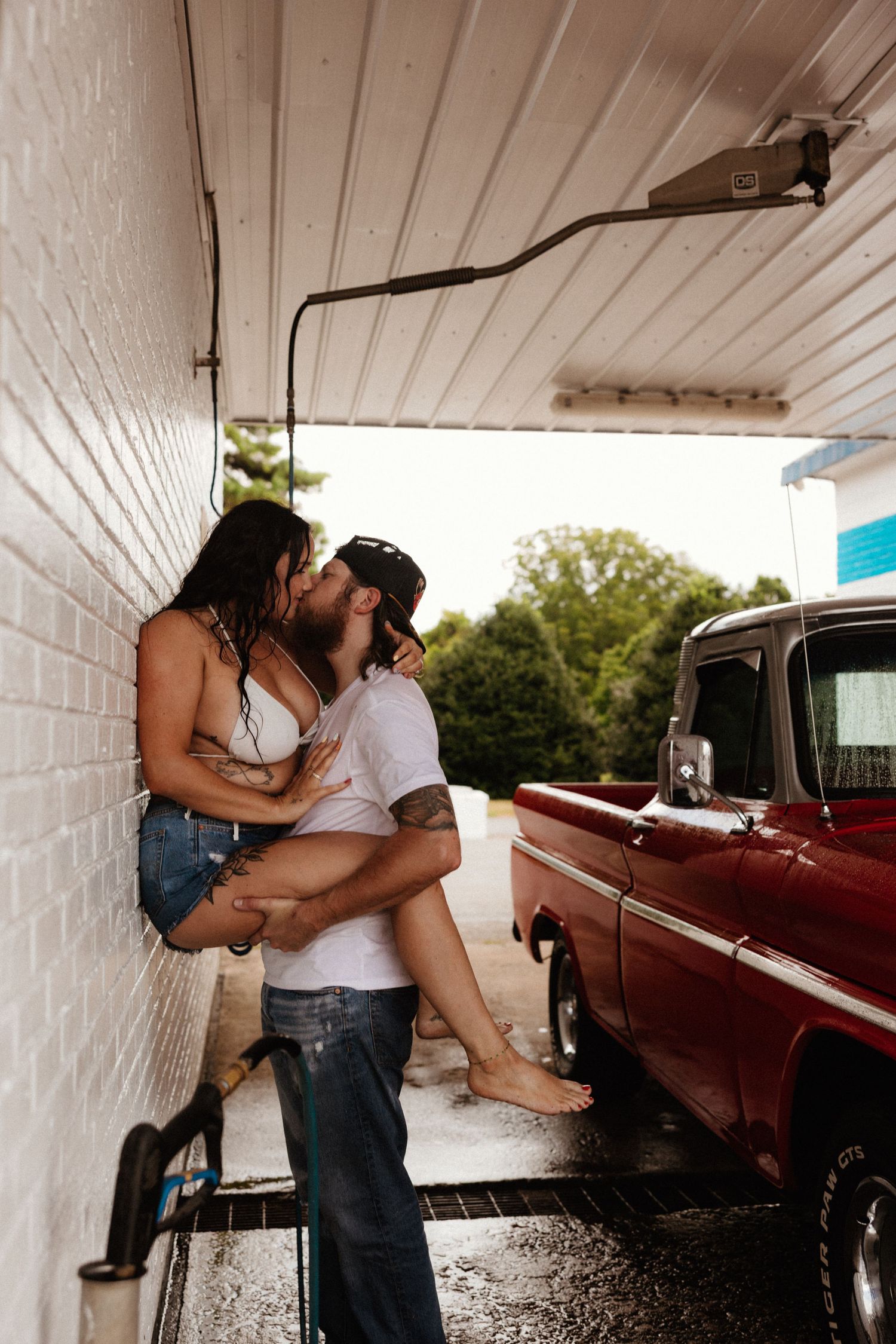 A romantic embrace against white brick walls with a classic red pickup truck in frame.