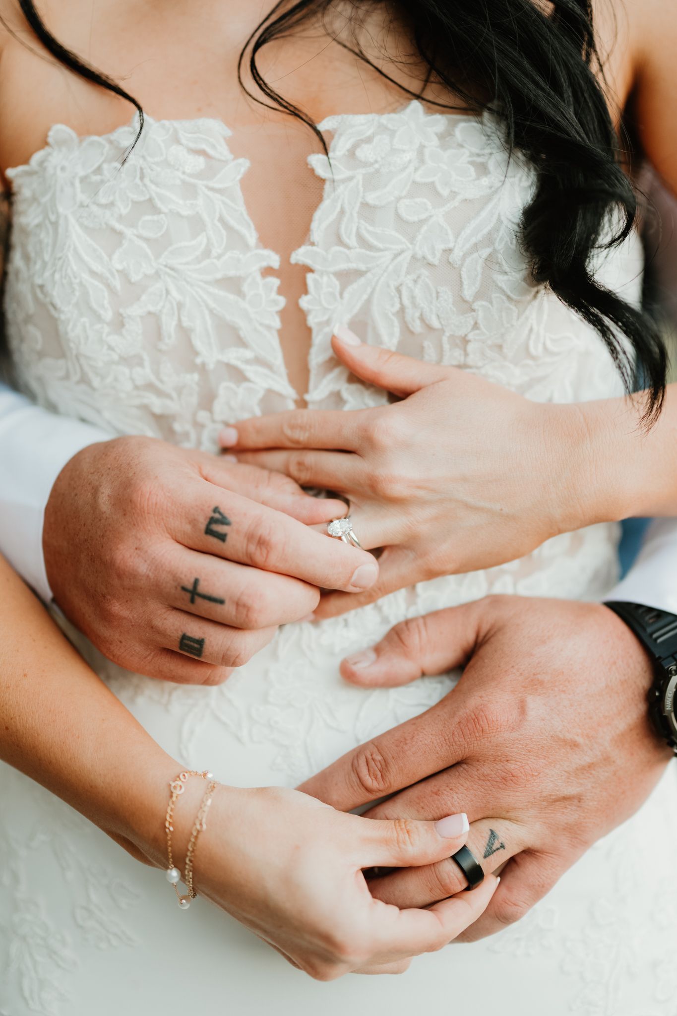 Close-up of newlywed hands with tattoos against a detailed white lace wedding dress.